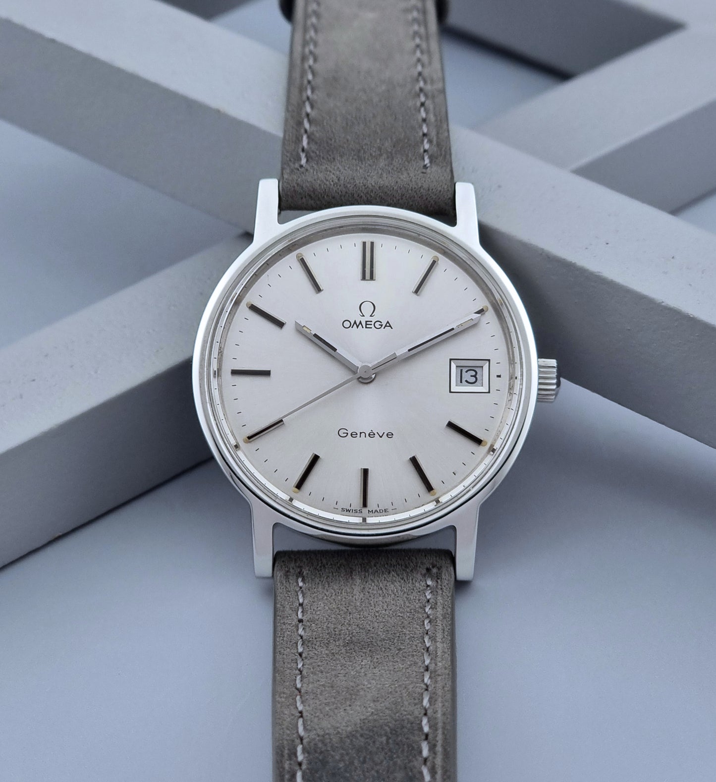 Vintage Omega Wristwatch Geneve 136.0099 with a grey leather strap on a grey background front view