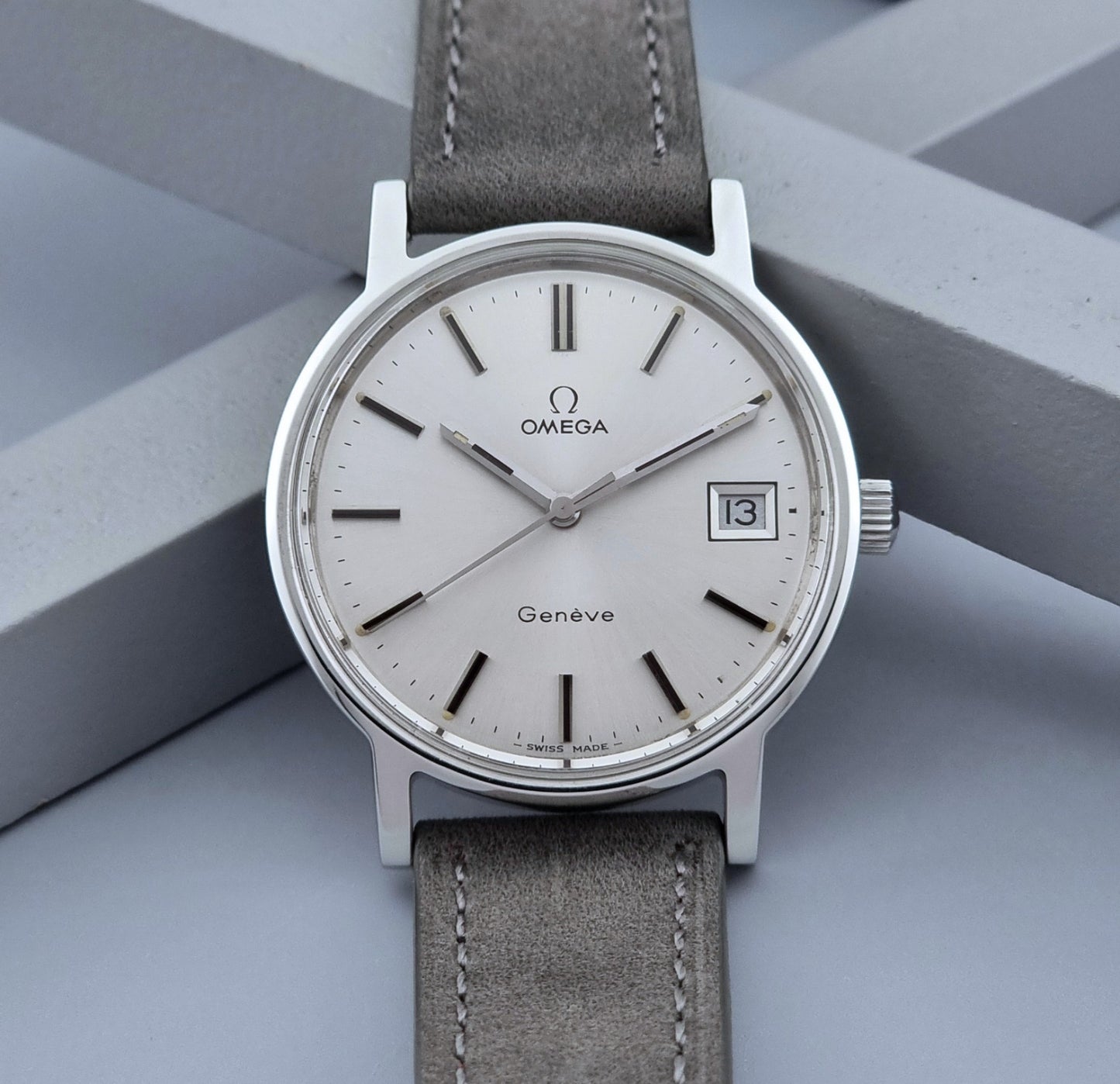 Vintage Omega Wristwatch Geneve 136.0099 with a grey leather strap on a grey background close up dial view