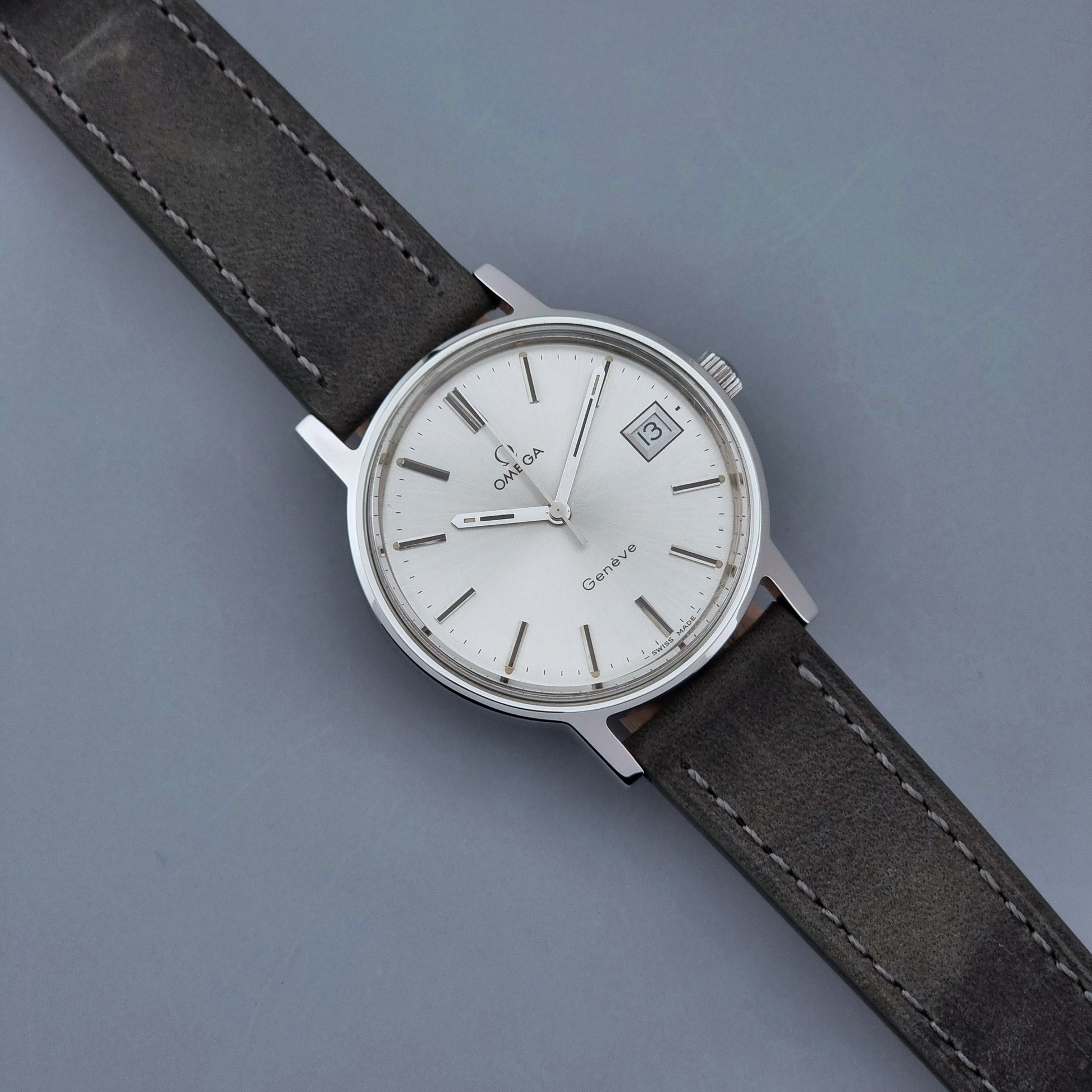 Vintage Omega Wristwatch Geneve 136.0099 with a grey leather strap on a grey background front