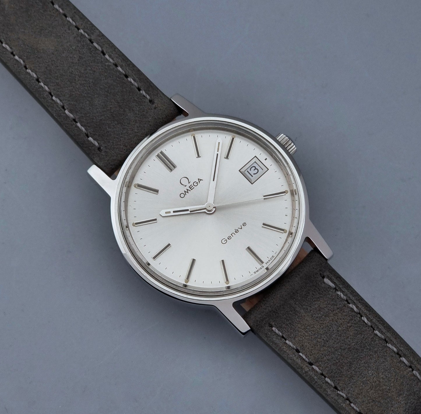 Vintage Omega Wristwatch Geneve 136.0099 with a grey leather strap on a grey background close dial view