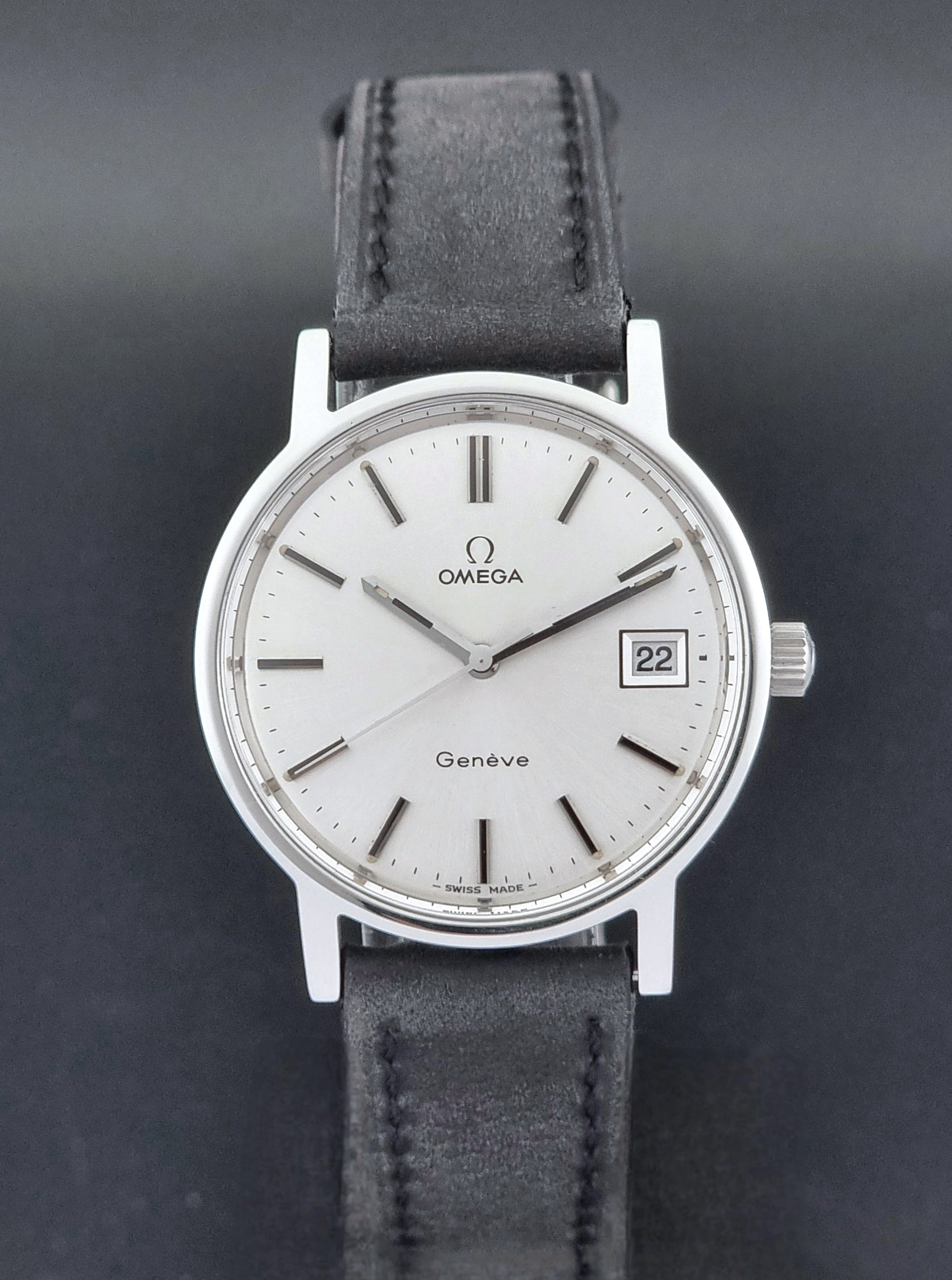 Vintage Omega Wristwatch Geneve 136.0099 with a black leather strap on a dark surface front view