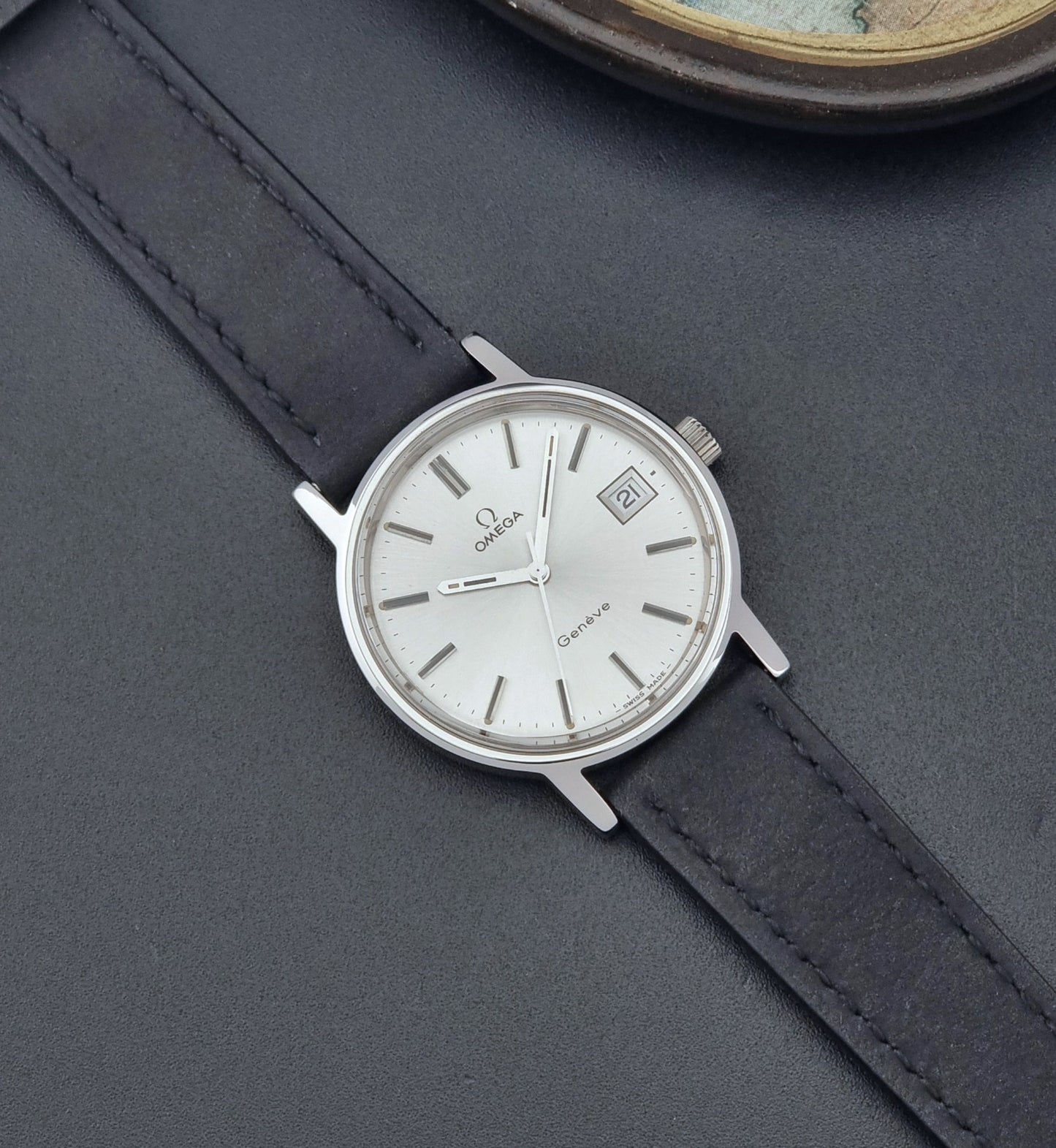 Vintage Omega Wristwatch Geneve 136.0099 with a black leather strap on a dark surface dial