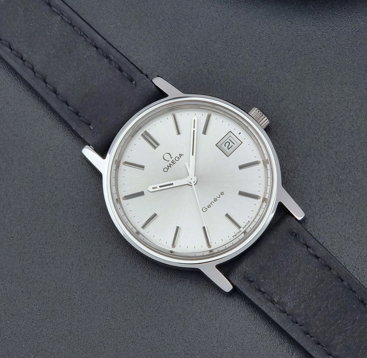 Vintage Omega Wristwatch Geneve 136.0099 with a black leather strap on a dark surface close dial view