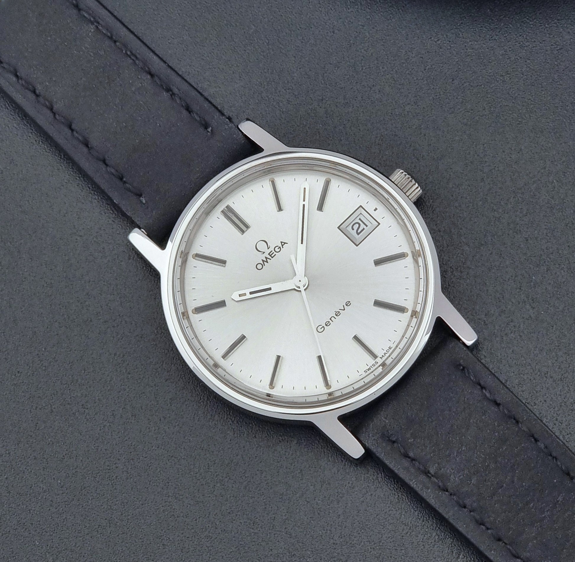 Vintage Omega Wristwatch Geneve 136.0099 with a black leather strap on a dark surface close dial view