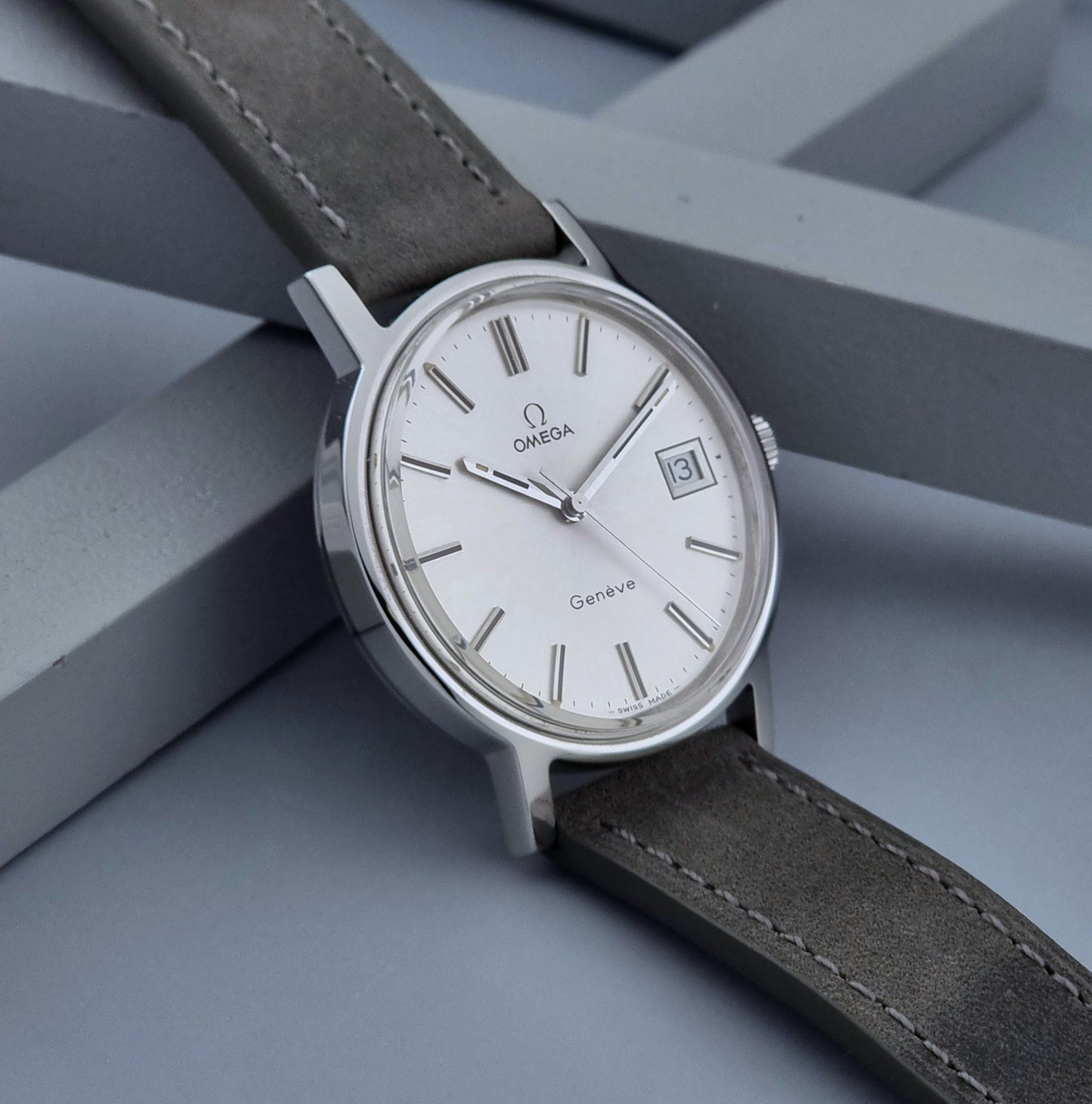 Vintage Omega Wristwatch Geneve 136.0099 with a grey leather strap on a grey background side view