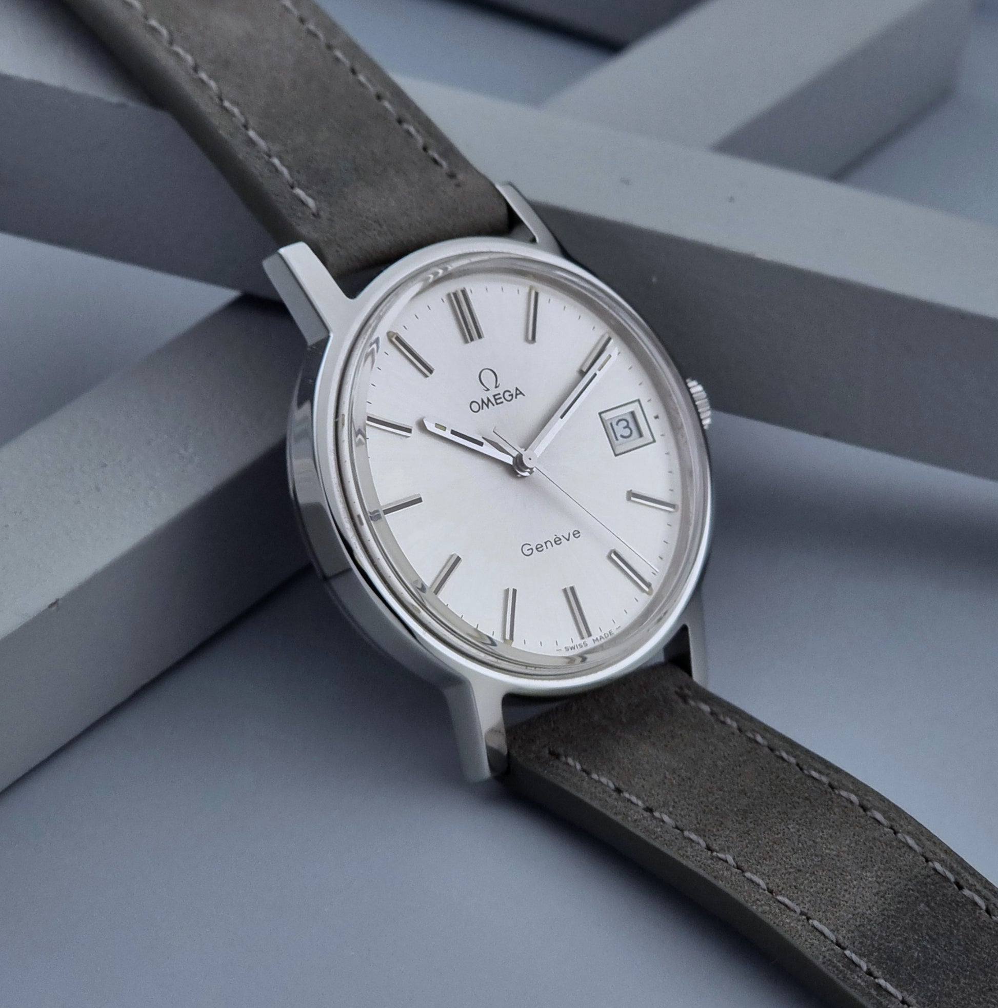 Vintage Omega Wristwatch Geneve 136.0099 with a grey leather strap on a grey background side view