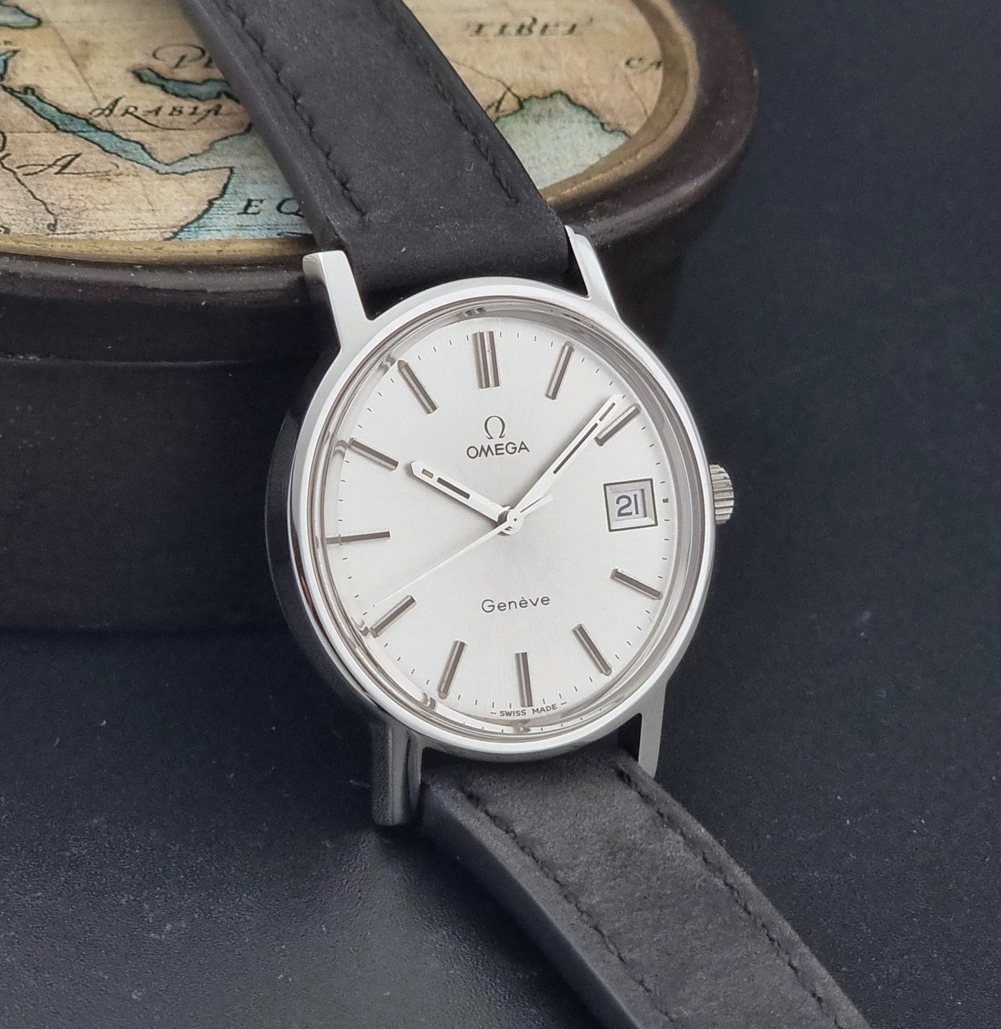 Vintage Omega Wristwatch Geneve 136.0099 with a black leather strap on a dark surface side view