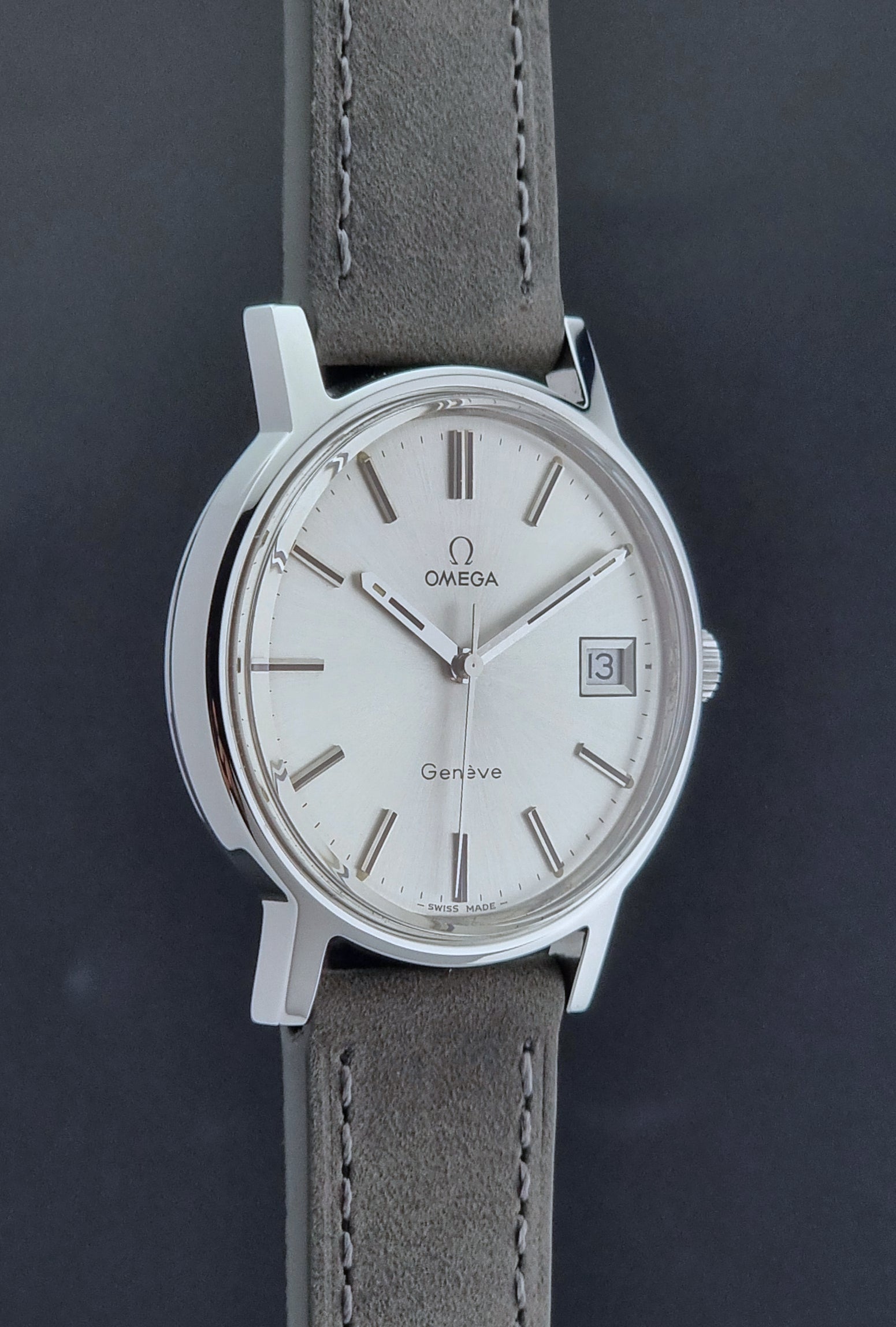 Vintage Omega Wristwatch Geneve 136.0099 with a grey leather strap on a grey background side profile view