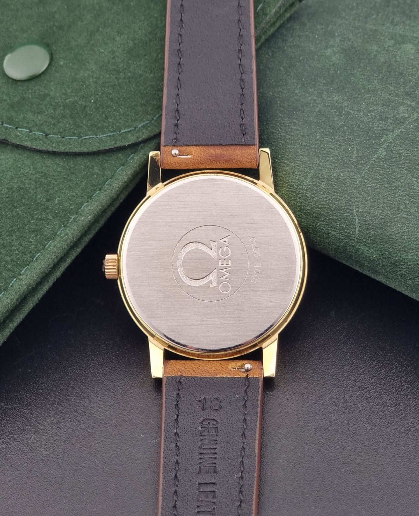 Vintage Omega Wristwatch Geneve 136.0104 with a gold case and brown strap on a dark background case back view
