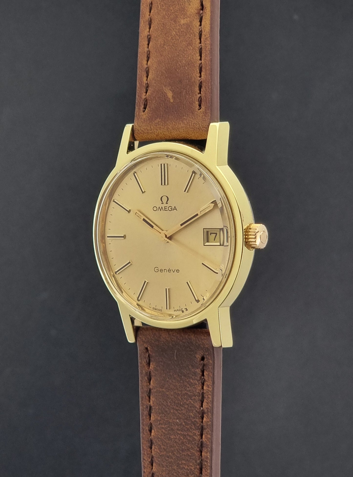 Vintage Omega Wristwatch Geneve 136.0104 with a gold case and brown strap on a dark background crown profile view