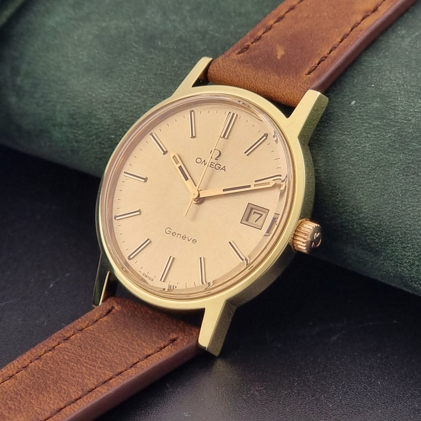 Vintage Omega Wristwatch Geneve 136.0104 with a gold case and brown strap on a dark background crown view