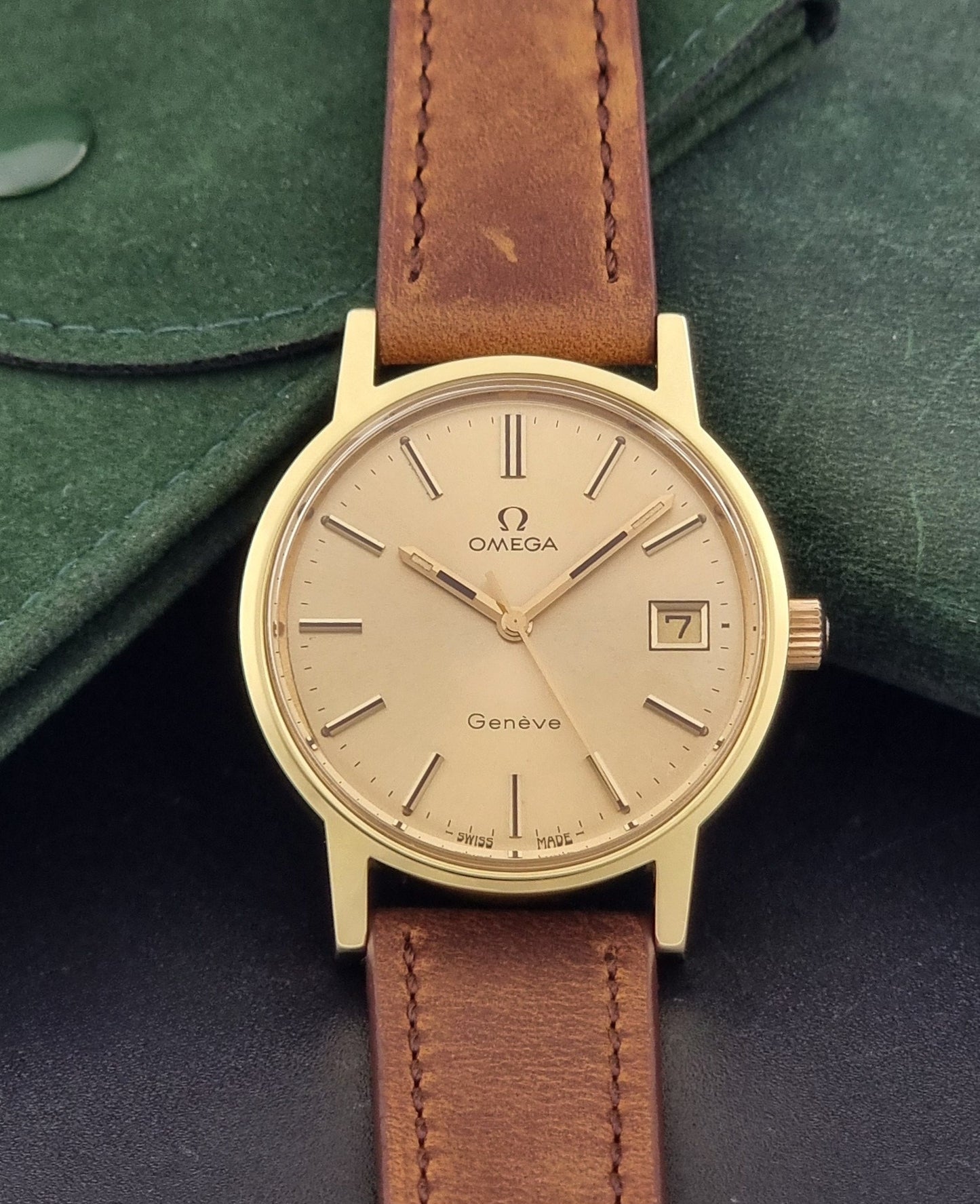Vintage Omega Wristwatch Geneve 136.0104 with a gold case and brown strap on a dark background dial view