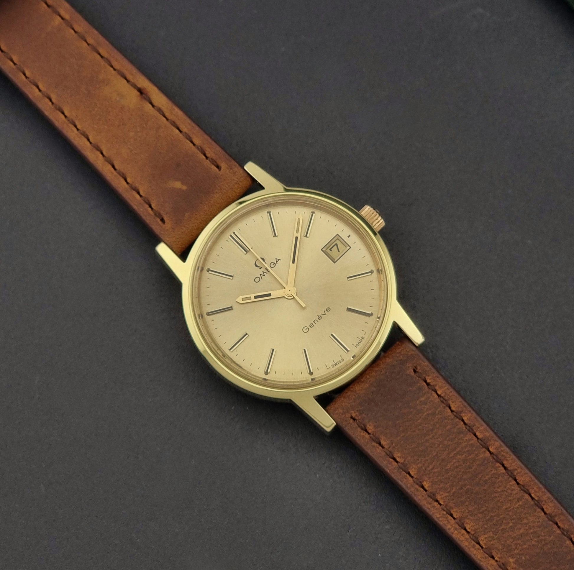 Vintage Omega Wristwatch Geneve 136.0104 with a gold case and brown strap on a dark background dial