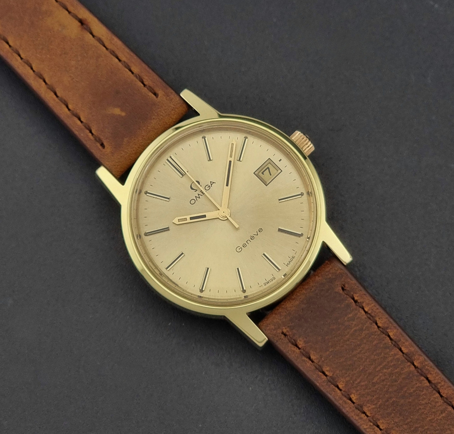 Vintage Omega Wristwatch Geneve 136.0104 with a gold case and brown strap on a dark background close up dial view