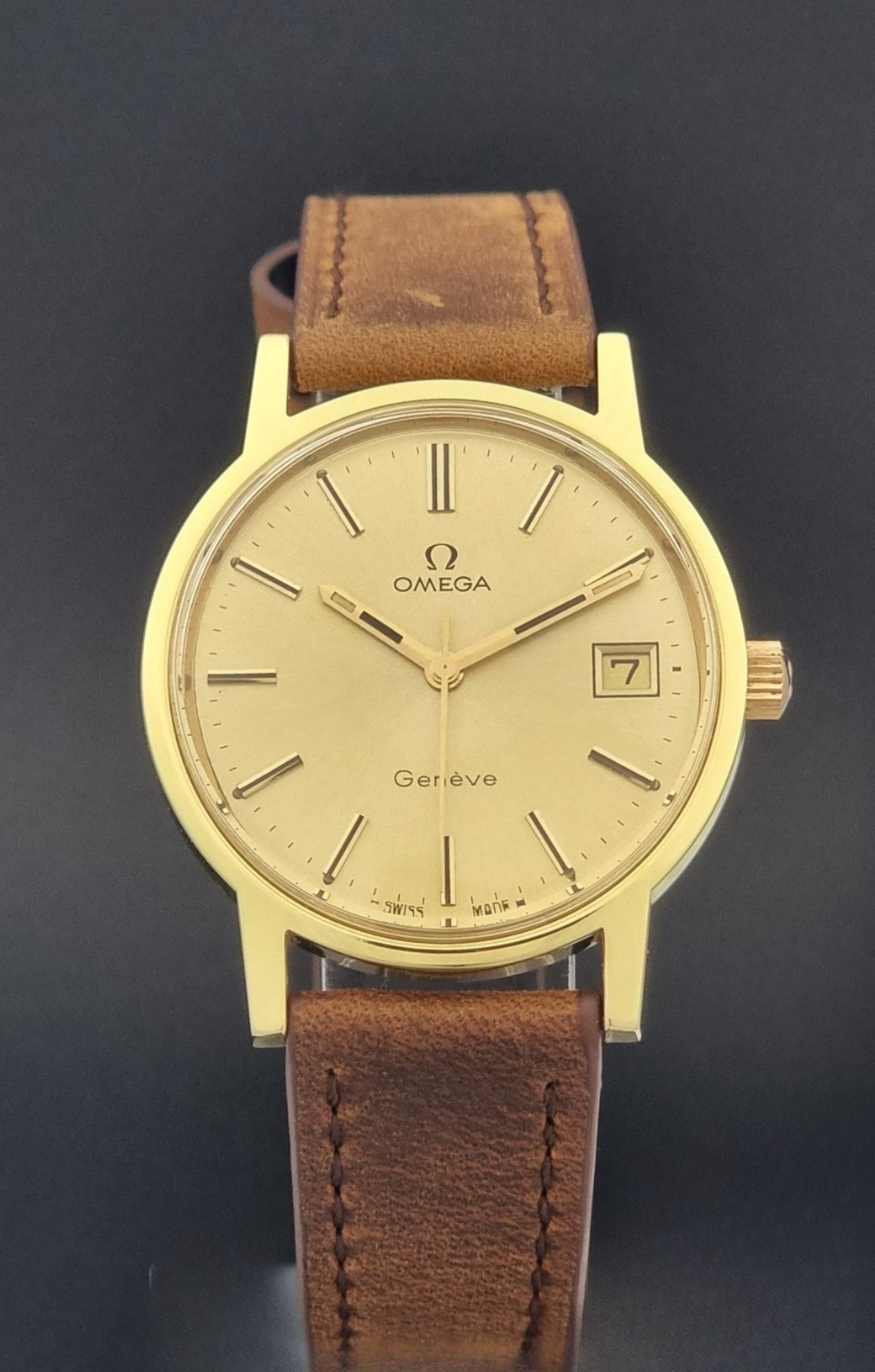 Vintage Omega Wristwatch Geneve 136.0104 with a gold case and brown strap on a dark background close dial view