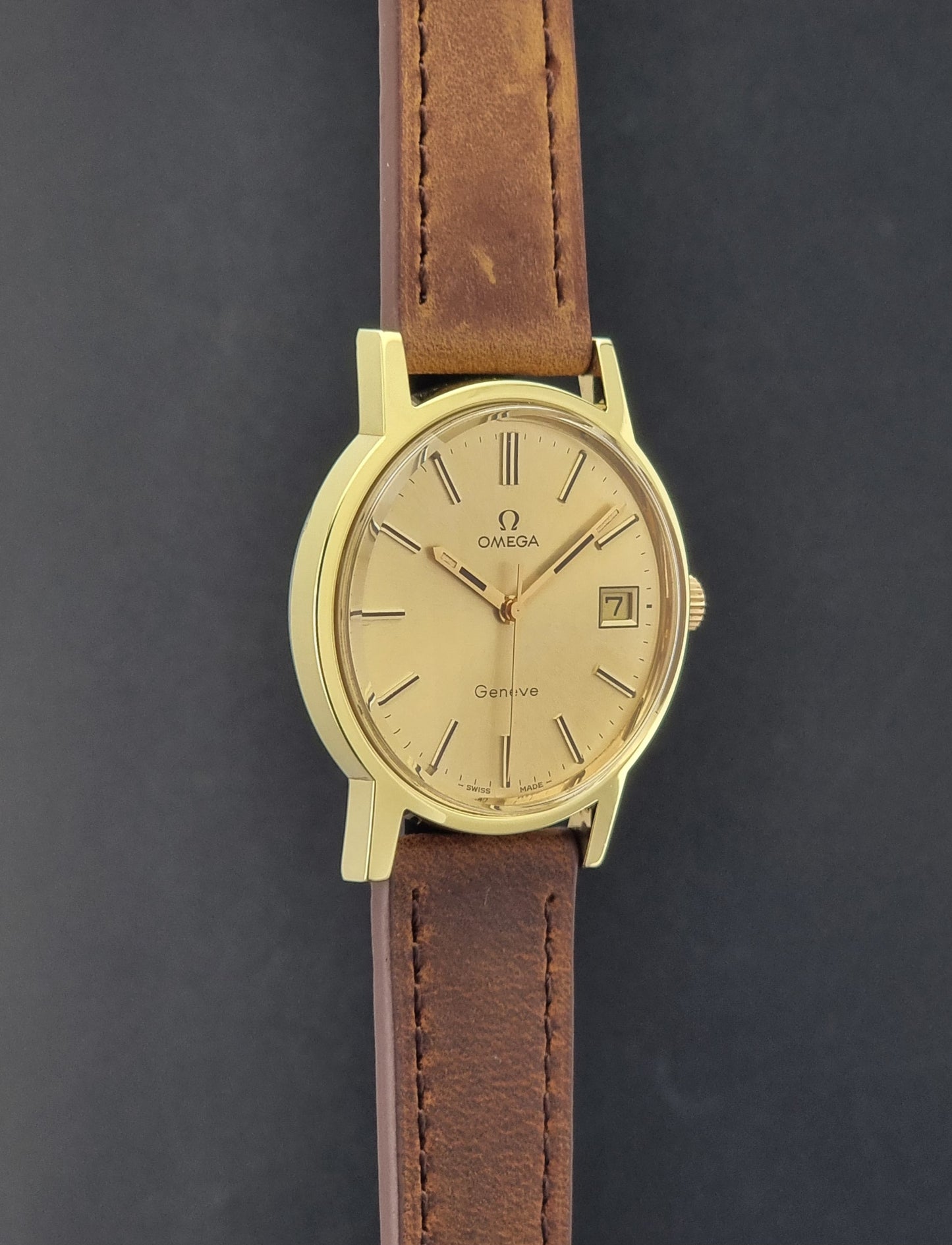 Vintage Omega Wristwatch Geneve 136.0104 with a gold case and brown strap on a dark background side profile view