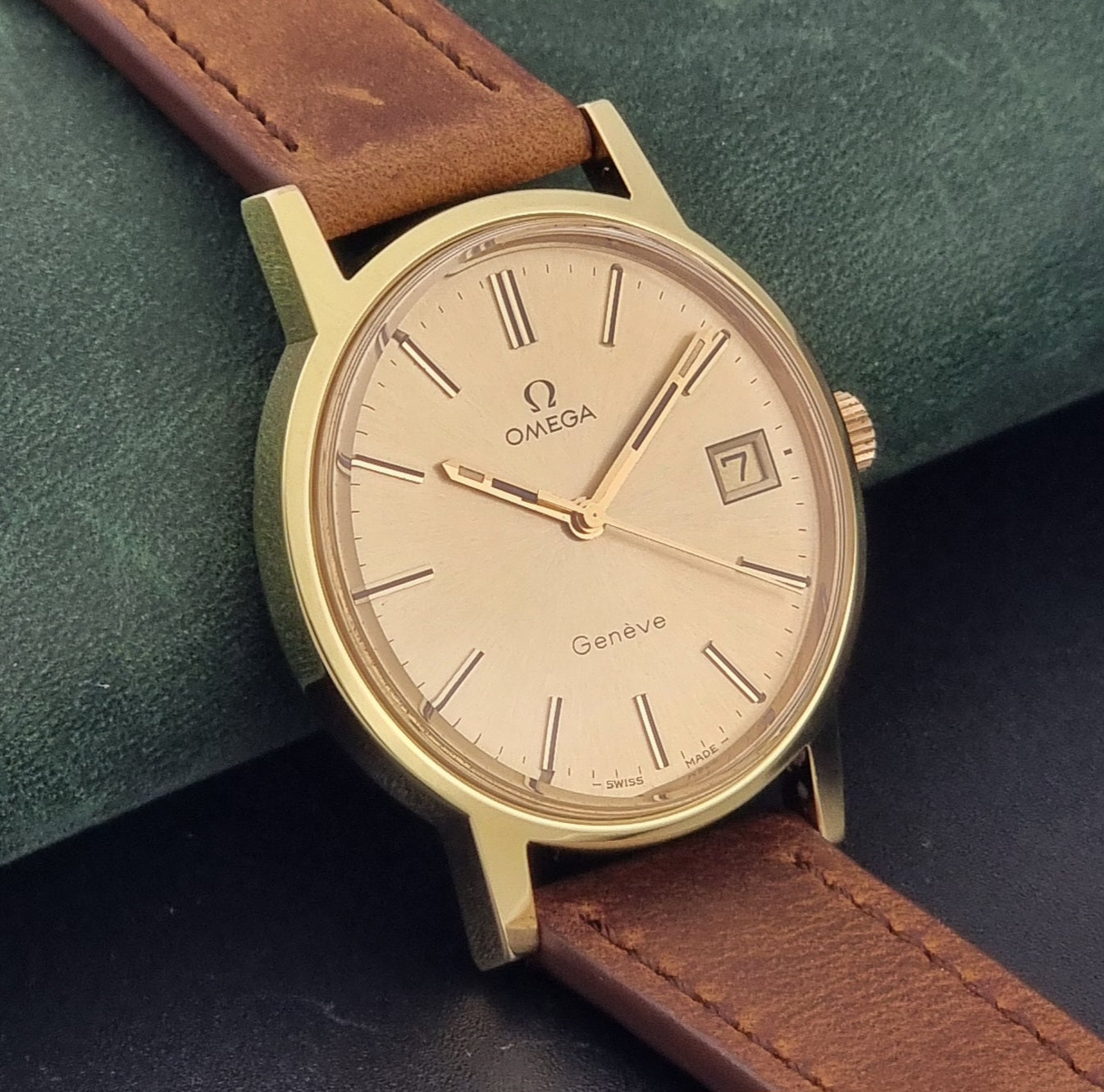 Vintage Omega Wristwatch Geneve 136.0104 with a gold case and brown strap on a dark background side view