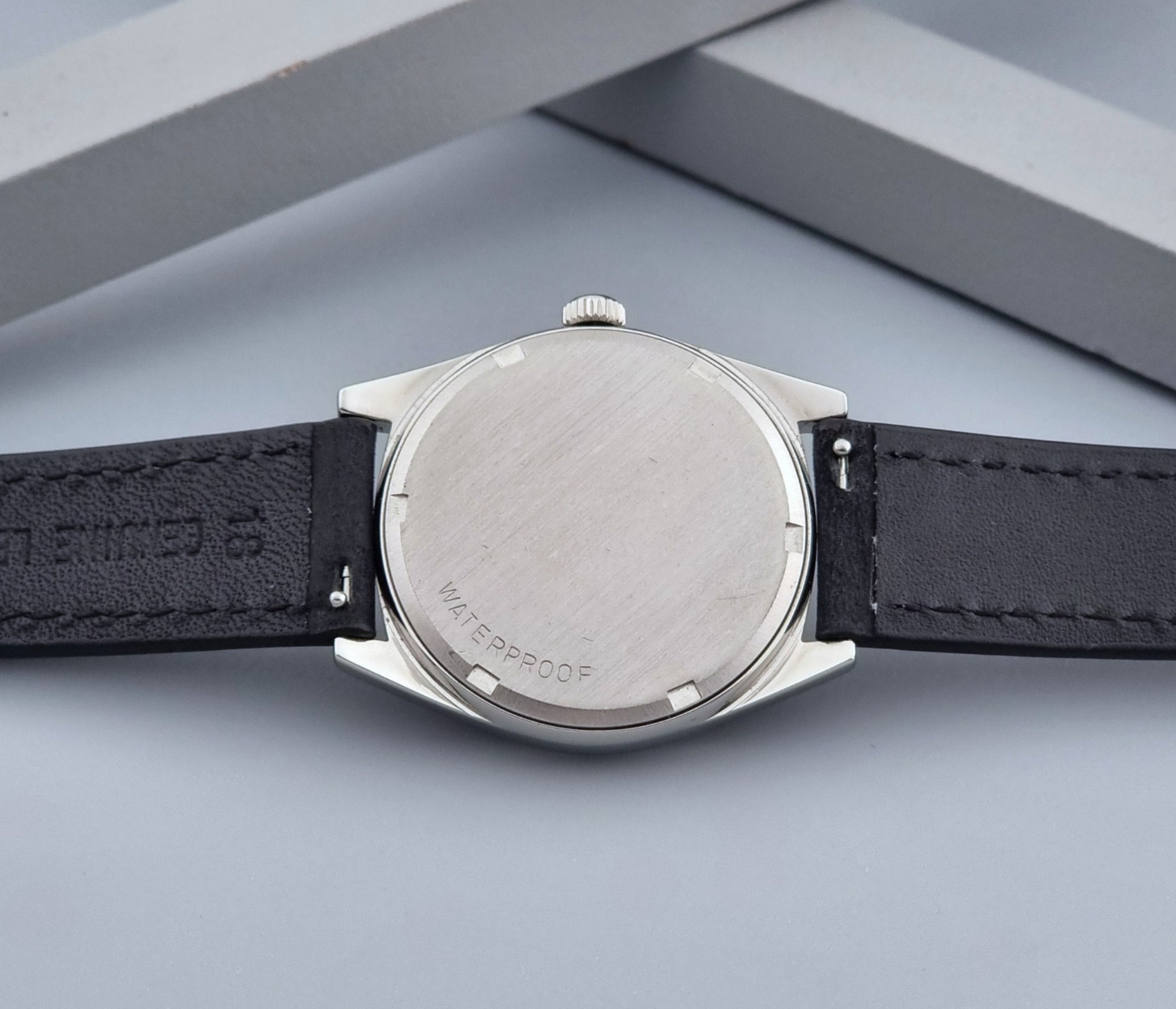 Vintage Omega watch Geneve 136.041 with a black leather strap on a dark gray background case back view