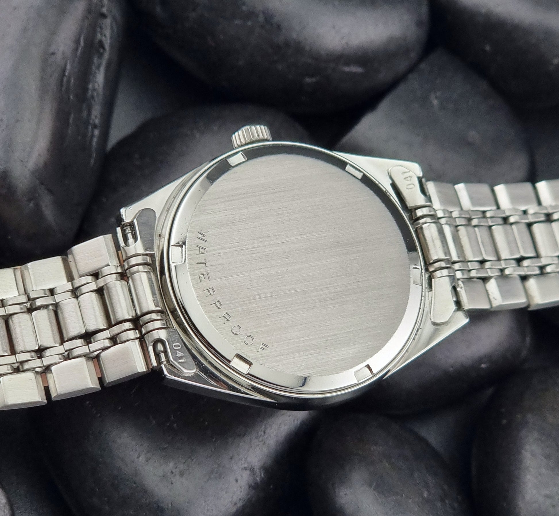 Vintage Omega Geneve watch with 'Waterproof' text on a dark stone surface