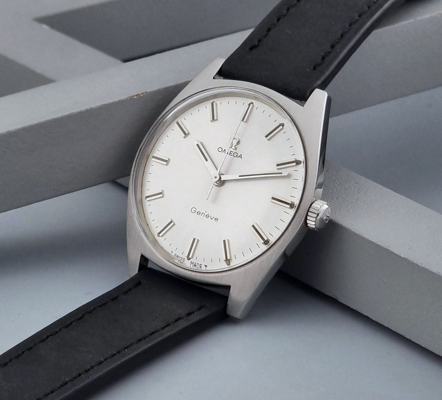 Vintage Omega watch Geneve 136.041 with a black leather strap on a dark gray background crown view