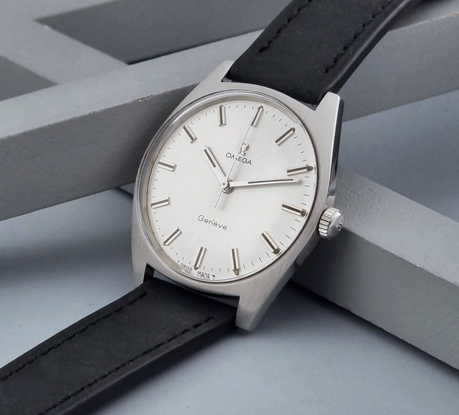 Vintage Omega watch Geneve 136.041 with a black leather strap on a dark gray background crown view