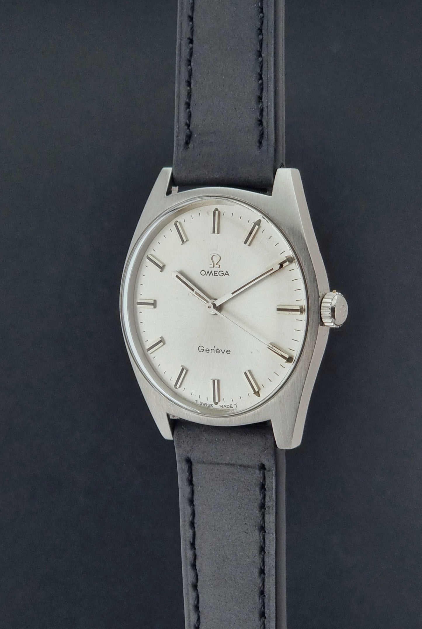 Vintage Omega watch Geneve 136.041 with a black leather strap on a dark gray background crown profile view