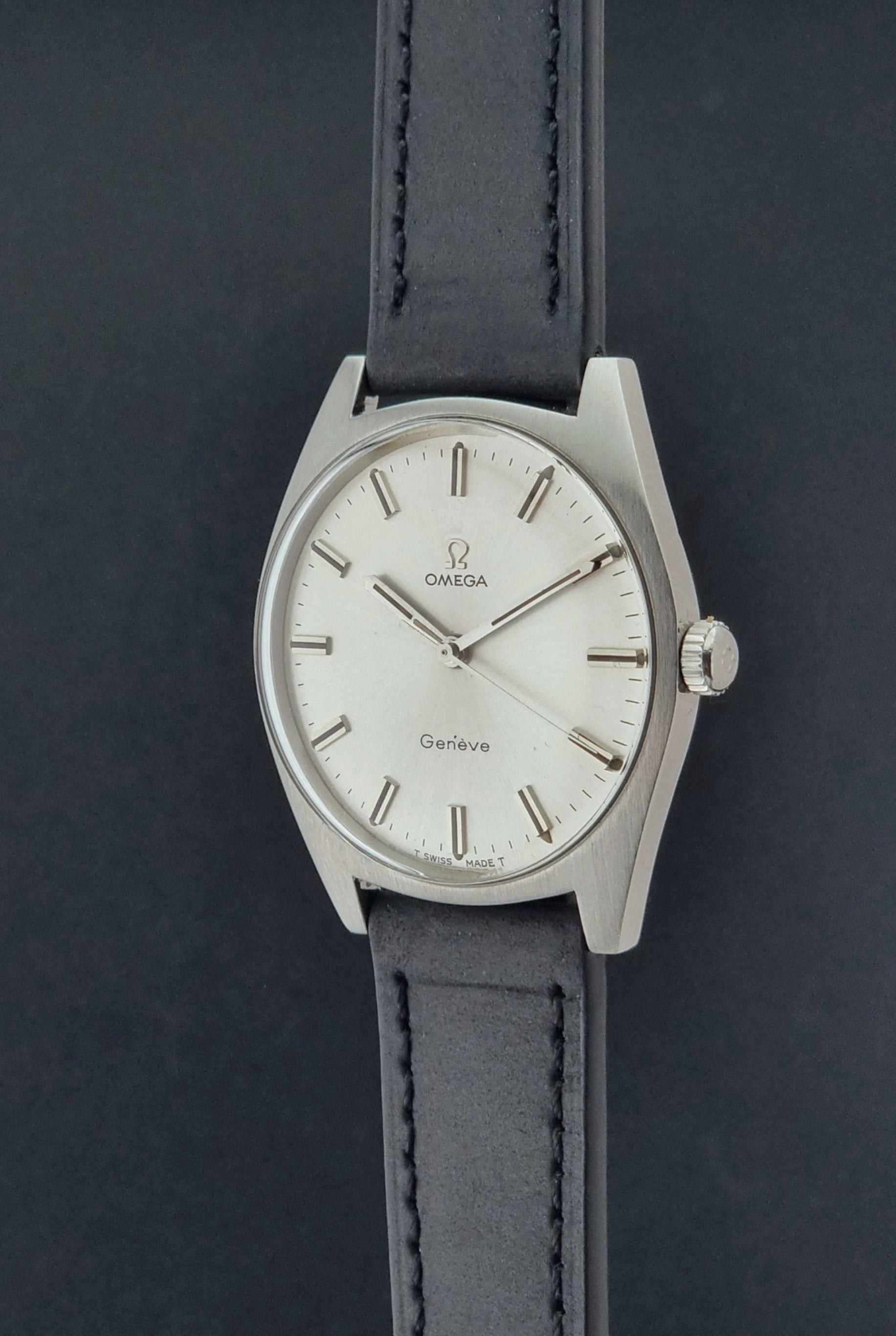 Vintage Omega watch Geneve 136.041 with a black leather strap on a dark gray background crown profile view