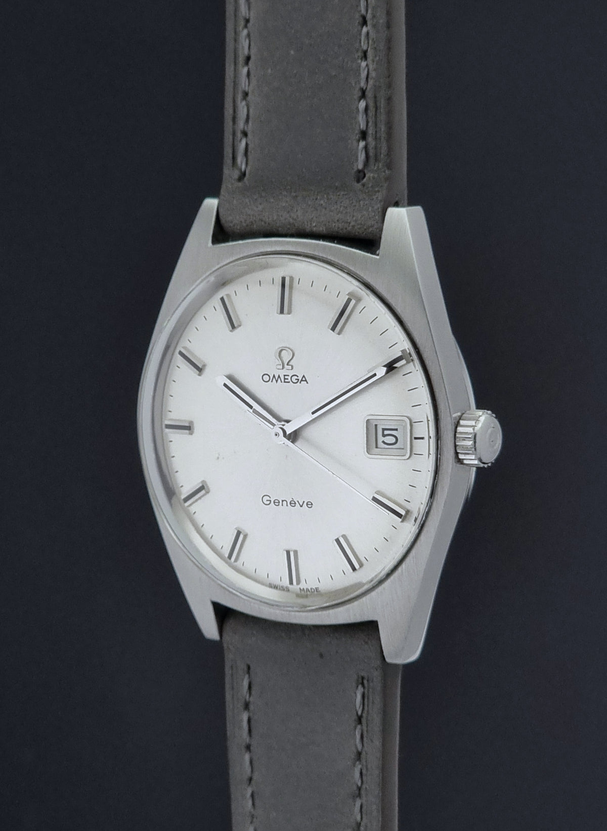 Vintage Omega Geneve 136.041 watch with a silver-toned metal case, white dial, and a dark gray leather strap, shown against a dark background.