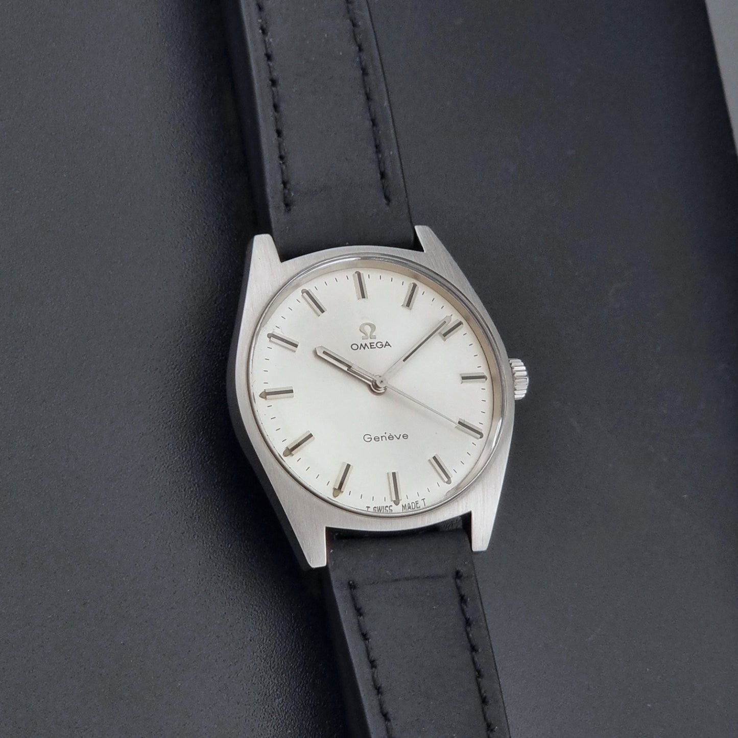 Vintage Omega watch Geneve 136.041 with a black leather strap on a dark gray background front view