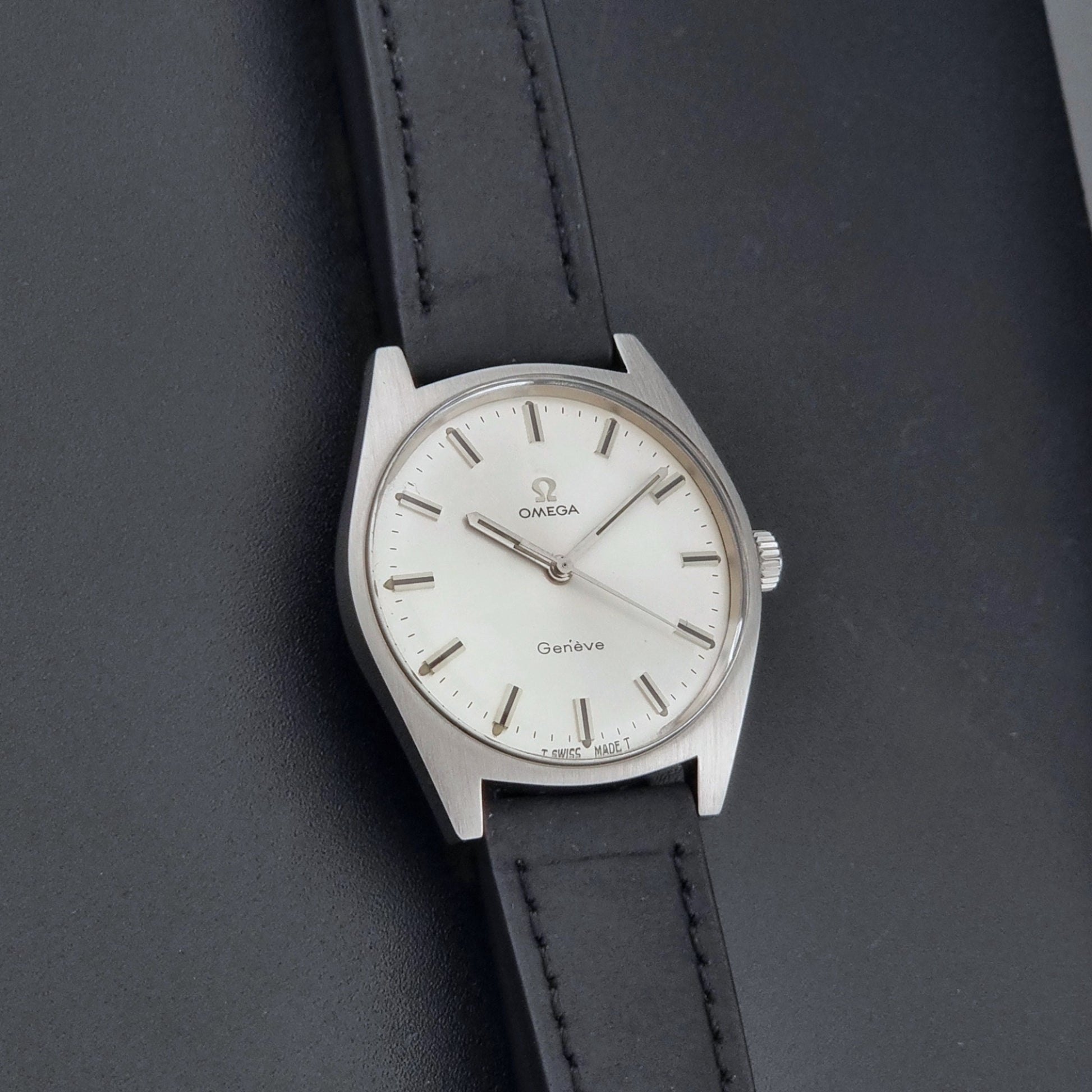 Vintage Omega watch Geneve 136.041 with a black leather strap on a dark gray background front view