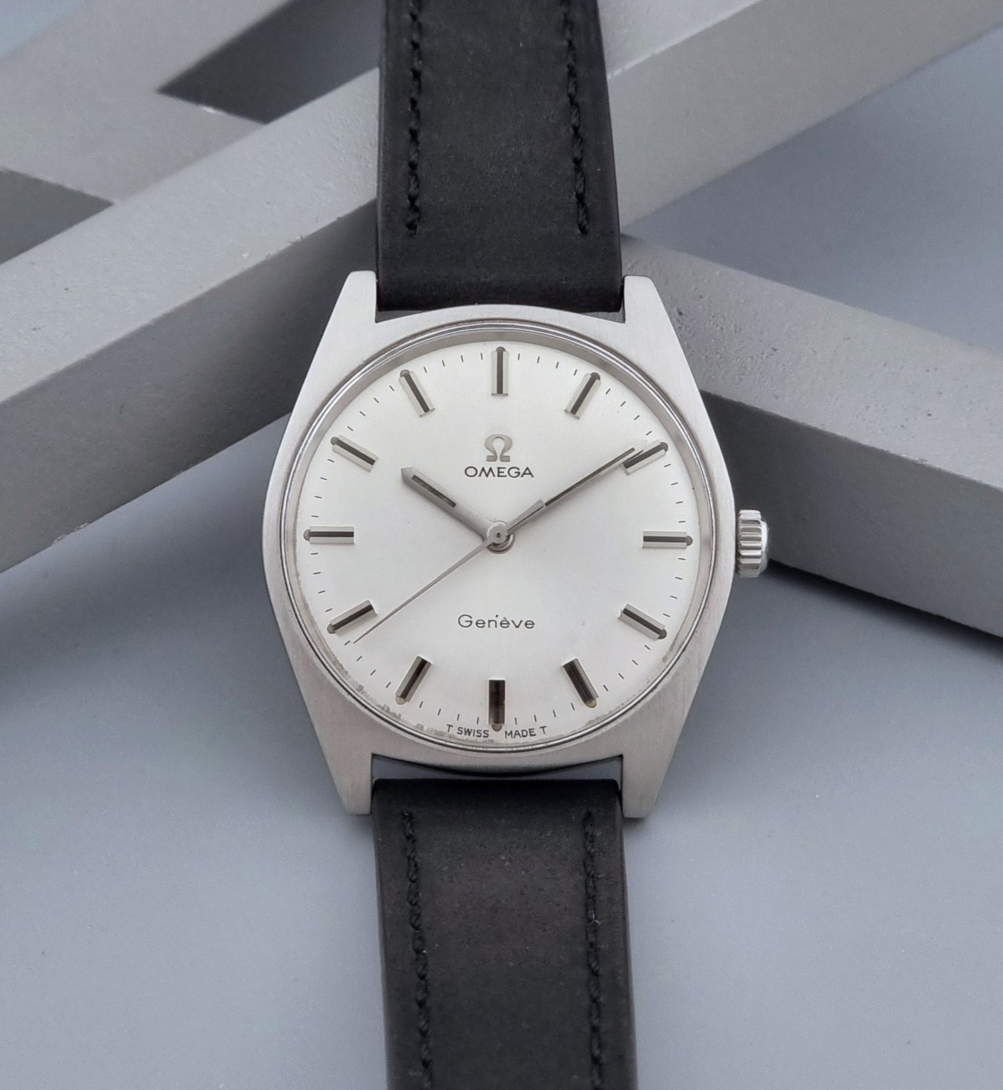 Vintage Omega watch Geneve 136.041 with a black leather strap on a dark gray background dial view