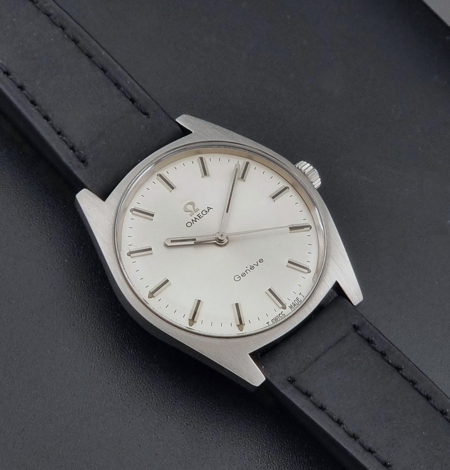 Vintage Omega watch Geneve 136.041 with a black leather strap on a dark gray background close up dial view