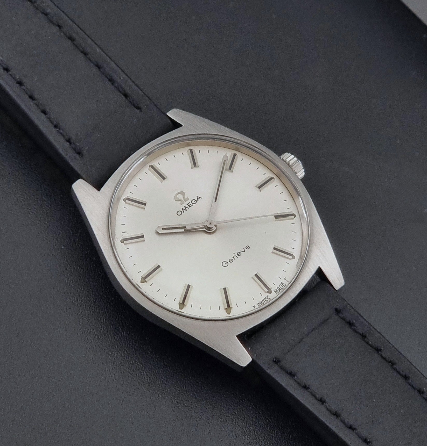 Vintage Omega watch Geneve 136.041 with a black leather strap on a dark gray background close up dial view
