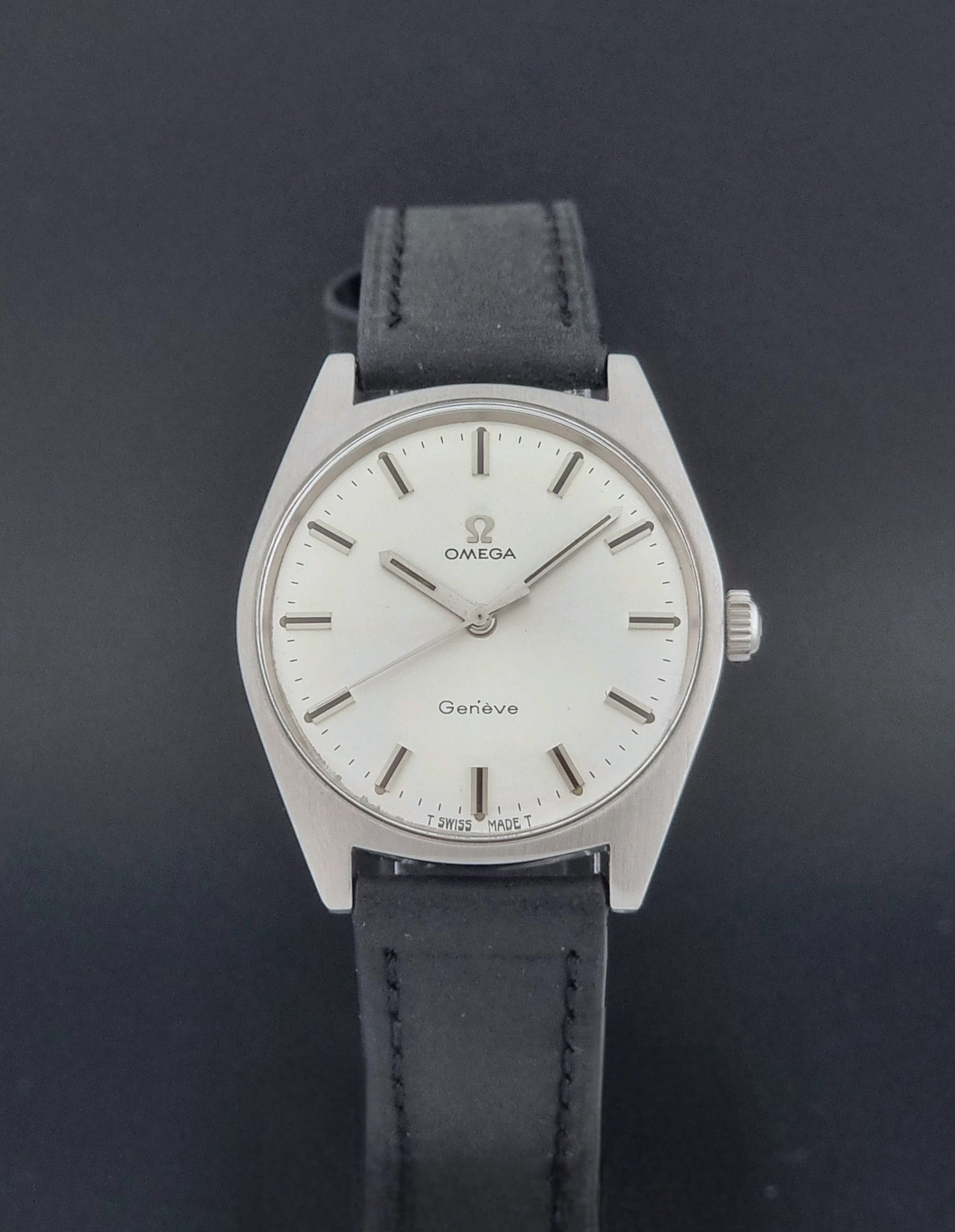 Vintage Omega watch Geneve 136.041 with a black leather strap on a dark gray background close dial view