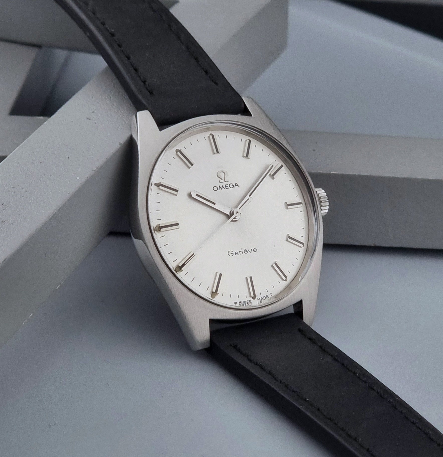 Vintage Omega watch Geneve 136.041 with a black leather strap on a dark gray background side view