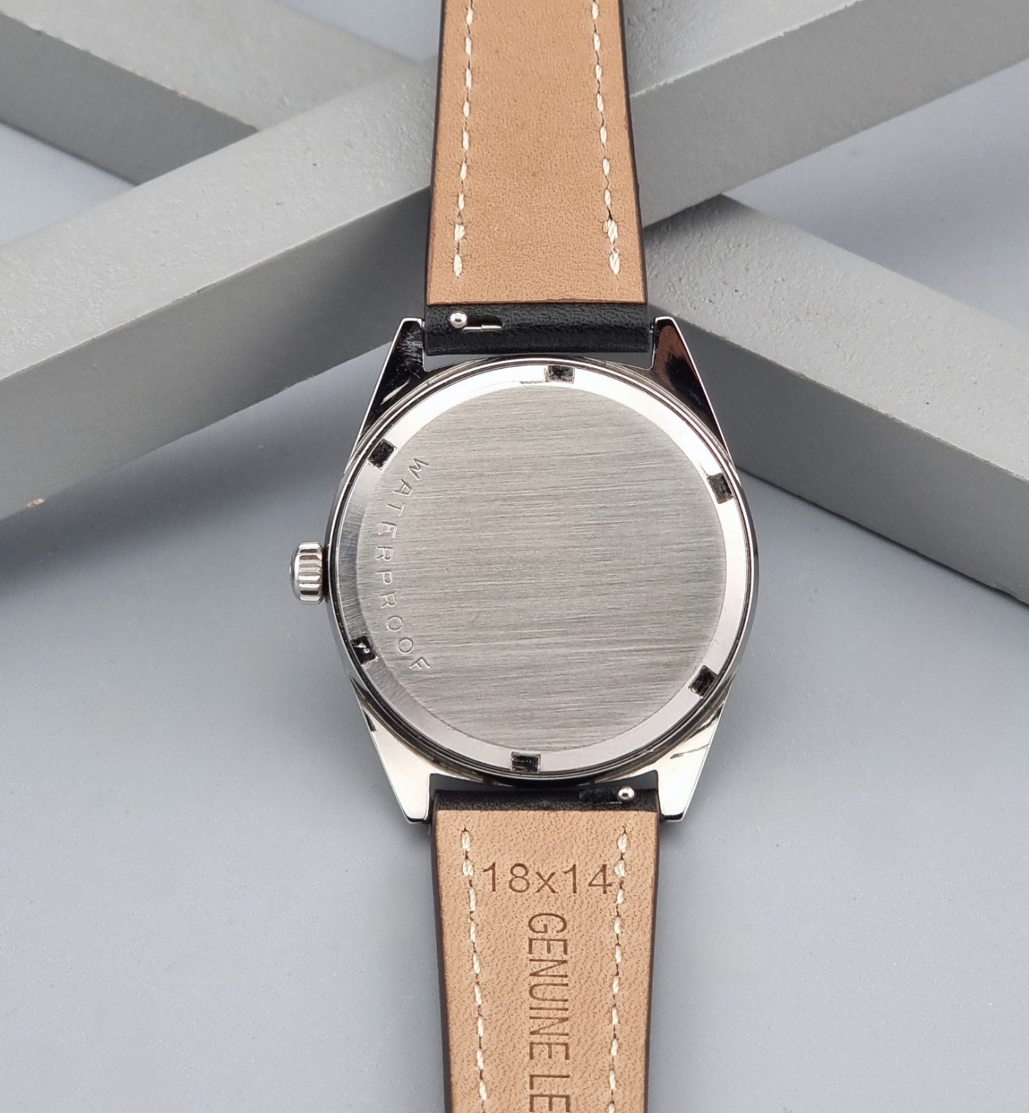 Vintage Omega watch Geneve 136.041 Co-signed Türler with a stainless steel case,  and a black leather strap with white stitching, shown on a gray background back view