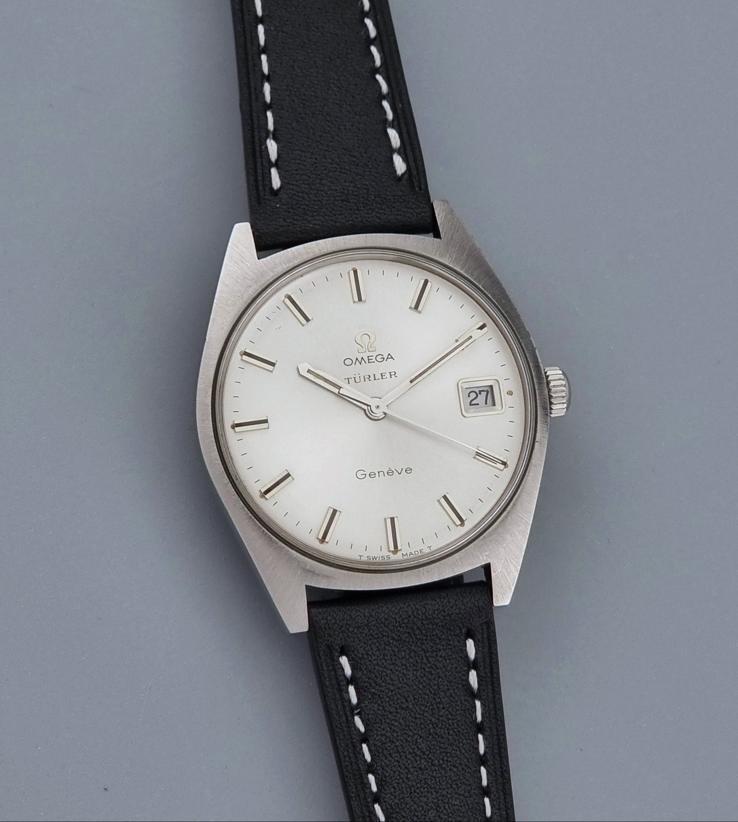 Vintage Omega watch Geneve 136.041 Co-signed Türler with a stainless steel case,  and a black leather strap with white stitching, shown on a gray background front view