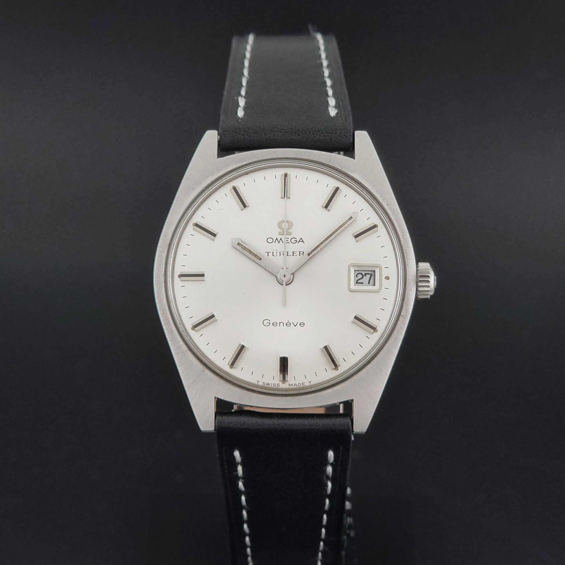 Vintage Omega watch Geneve 136.041 Co-signed Türler with a stainless steel case,  and a black leather strap with white stitching, shown on a gray background close dial view