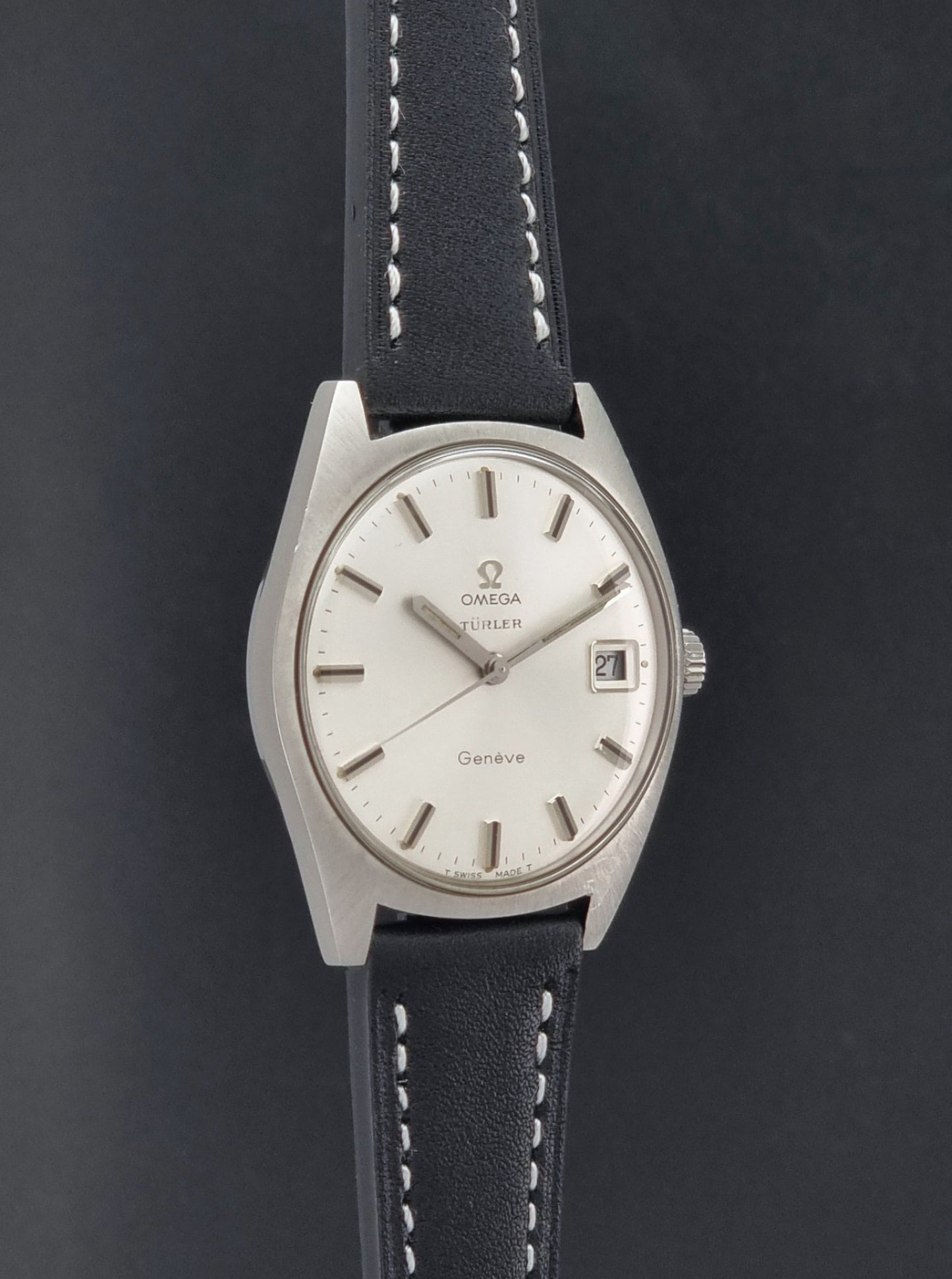Vintage Omega watch Geneve 136.041 Co-signed Türler with a stainless steel case,  and a black leather strap with white stitching, shown on a gray background side profile view