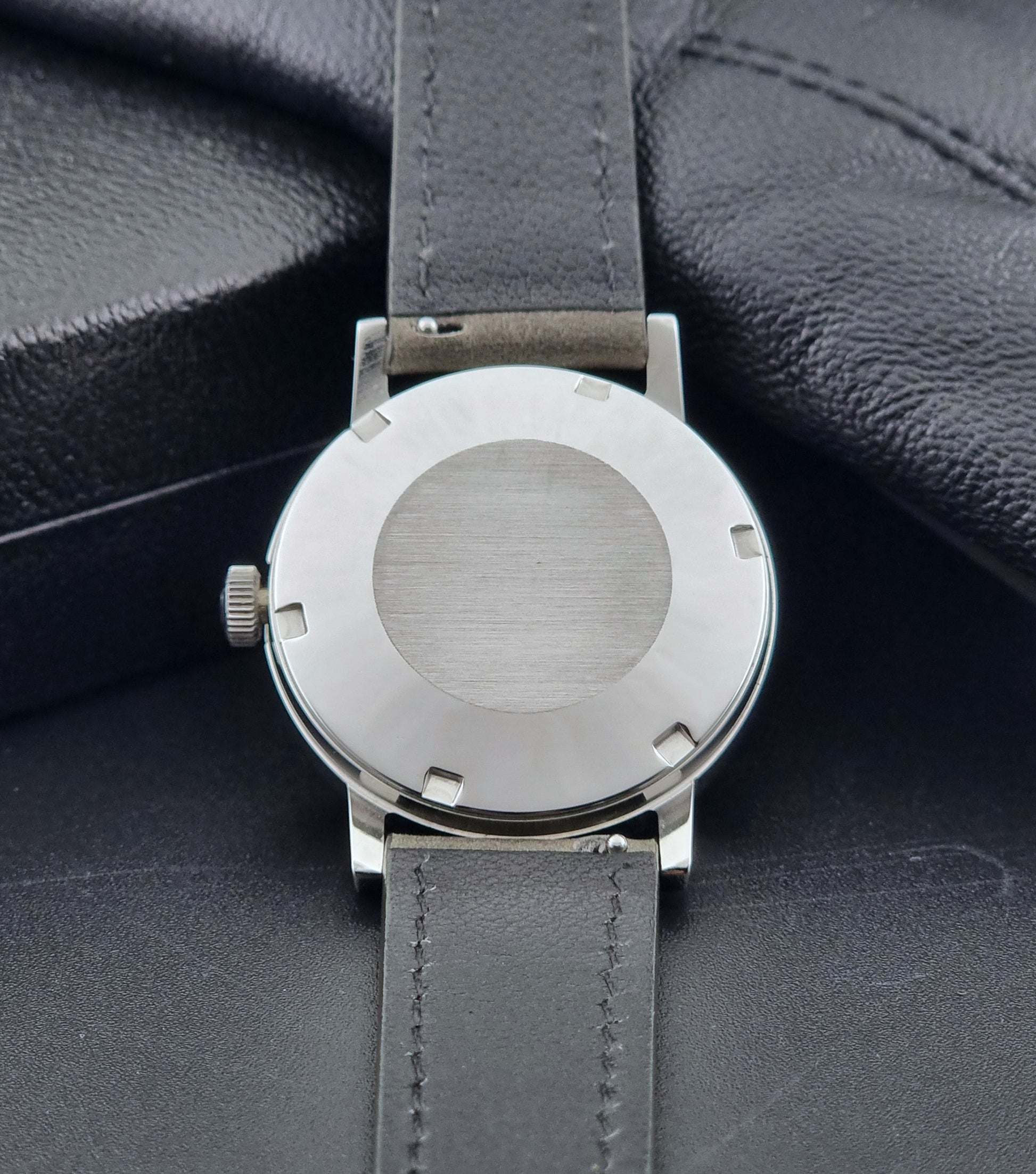 Vintage Omega Wristwatch Geneve 166.0098 with grey leather strap on a dark textured surface case back view