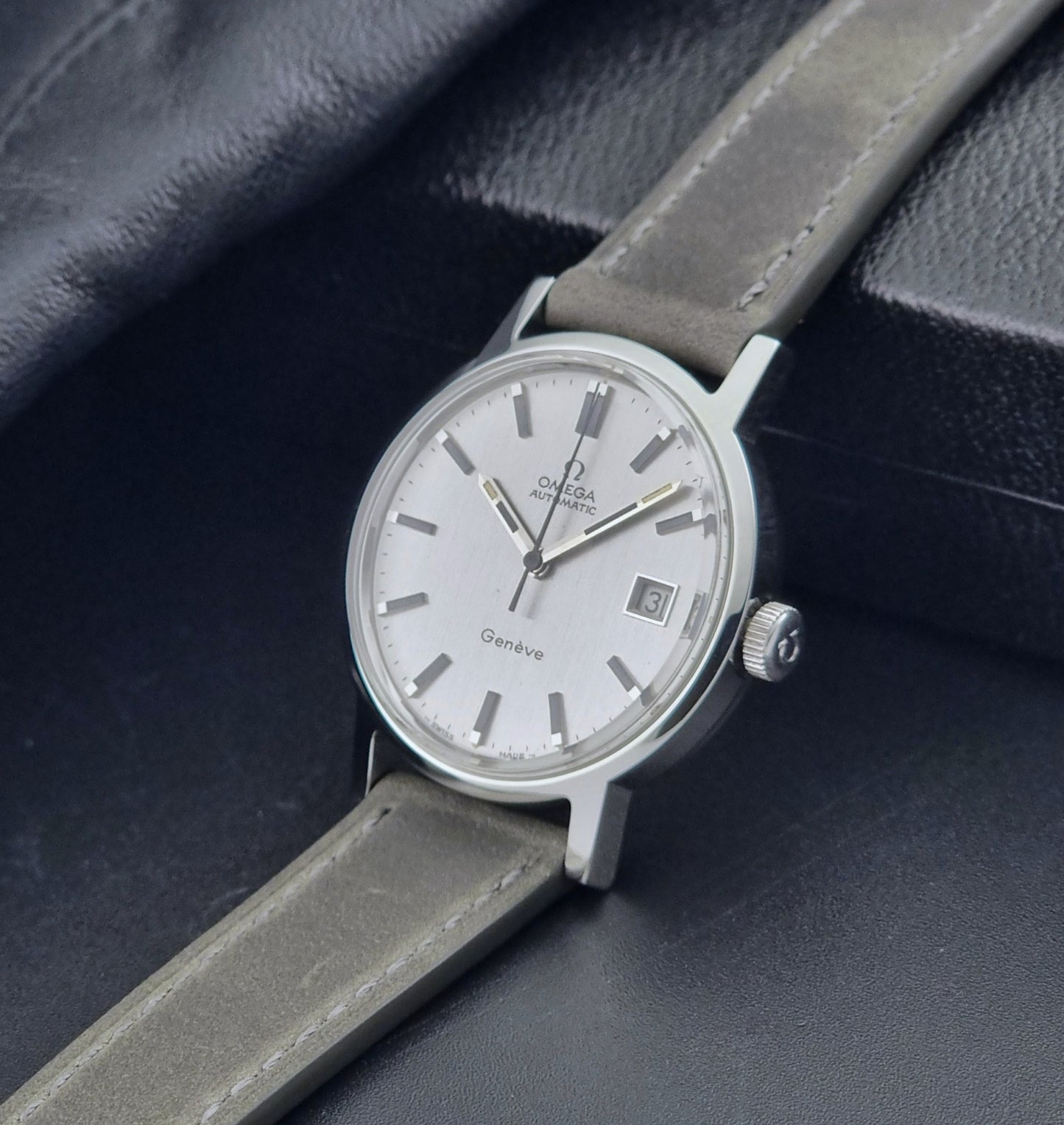 Vintage Omega Wristwatch Geneve 166.0098 with grey leather strap on a dark textured surface crown view