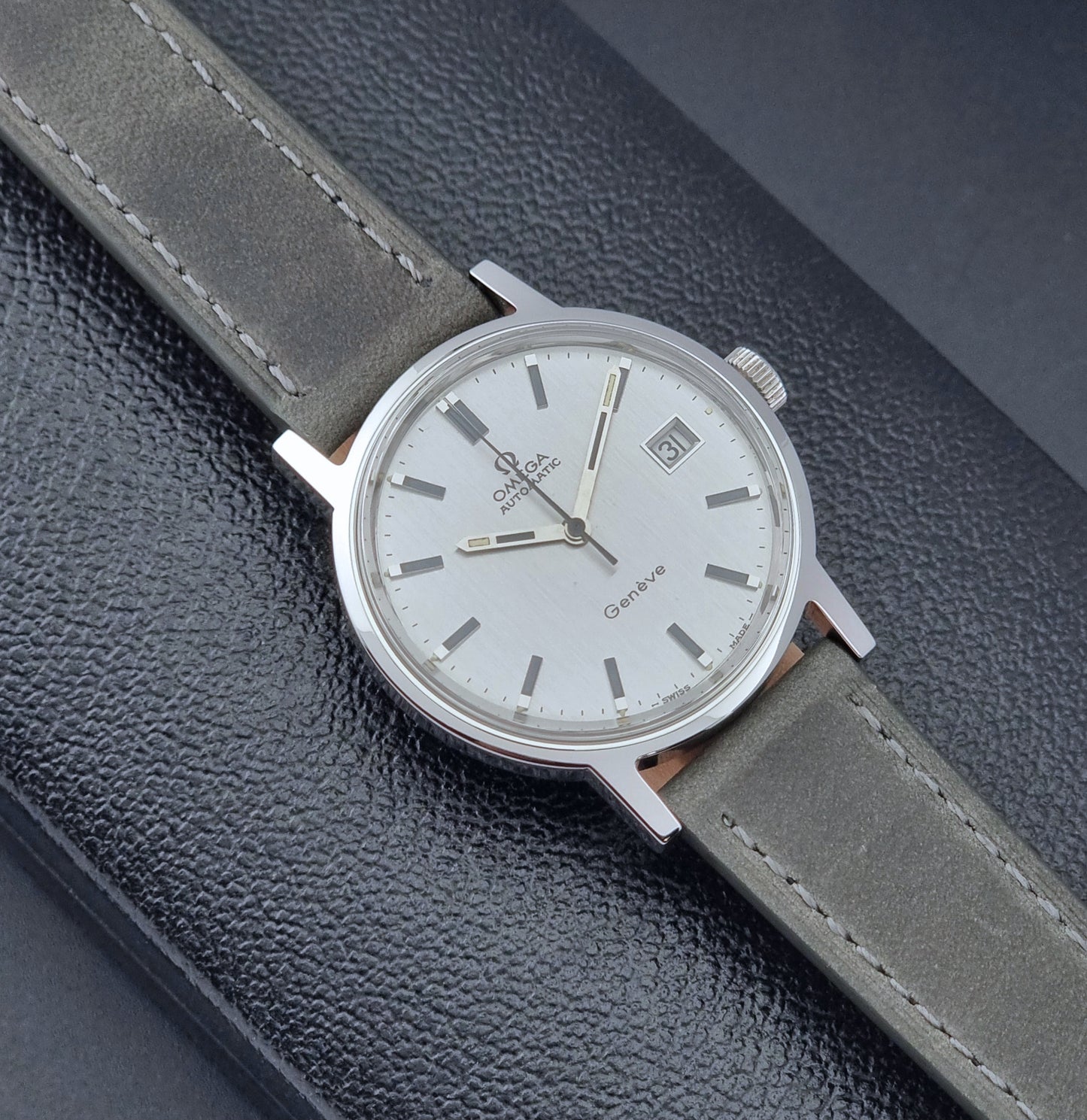 Vintage Omega Wristwatch Geneve 166.0098 with grey leather strap on a dark textured surface front