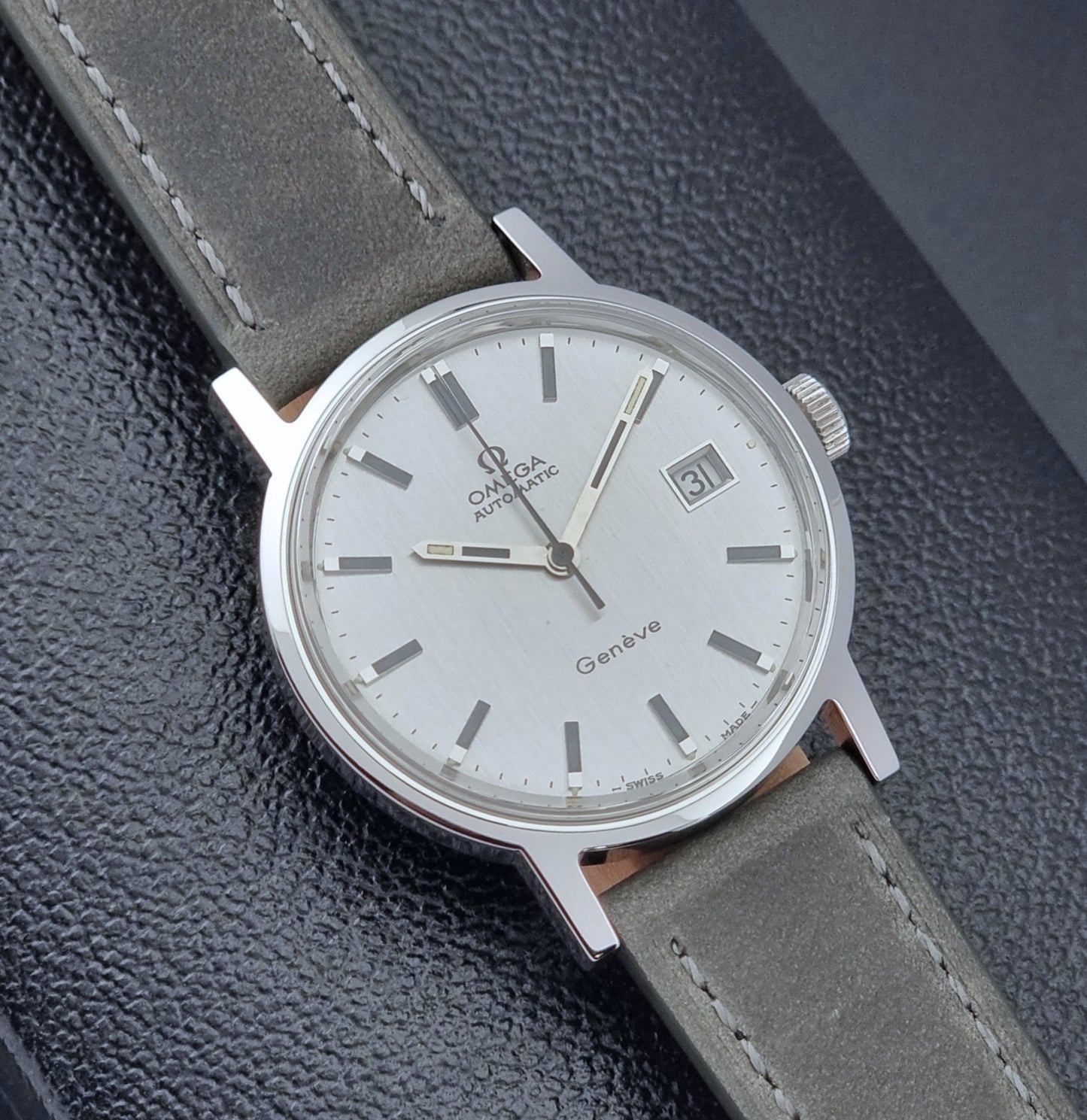 Vintage Omega Wristwatch Geneve 166.0098 with grey leather strap on a dark textured surface close dial view