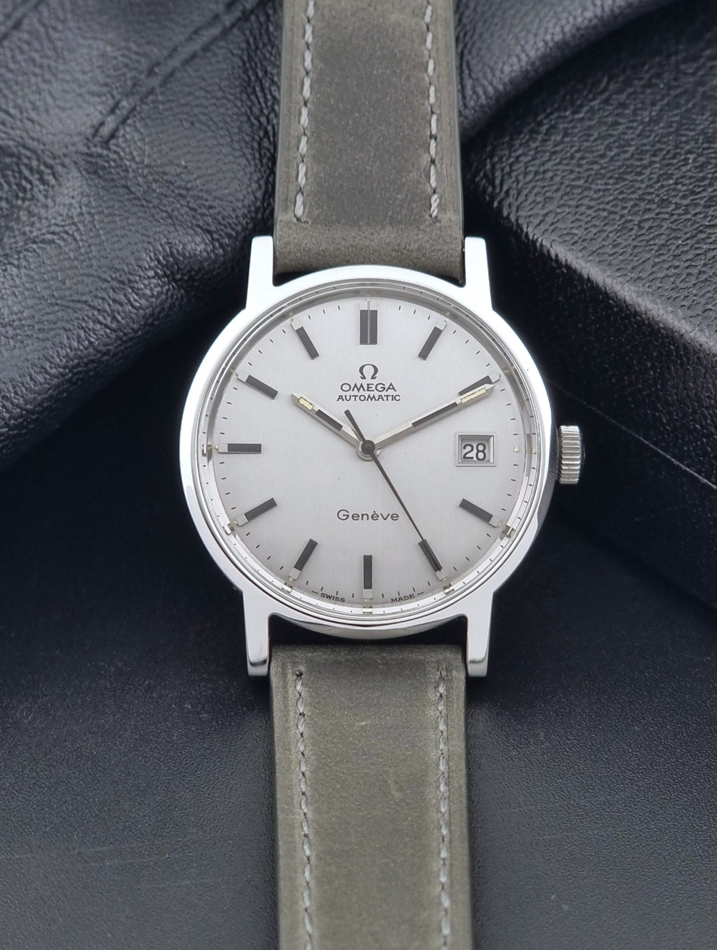 Vintage Omega Wristwatch Geneve 166.0098 with grey leather strap on a dark textured surface front view