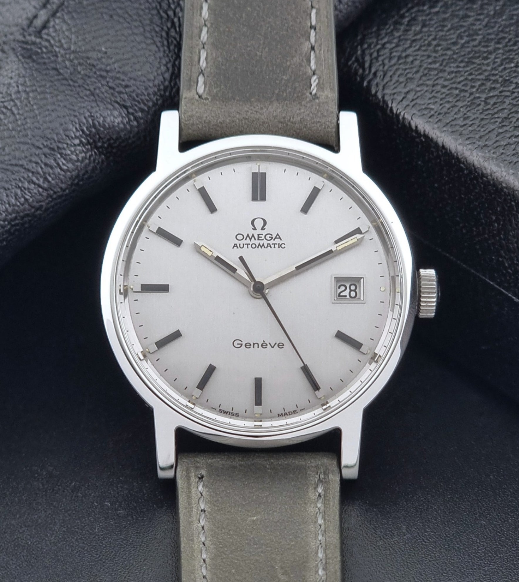 Vintage Omega Wristwatch Geneve 166.0098 with grey leather strap on a dark textured surface close up dial view