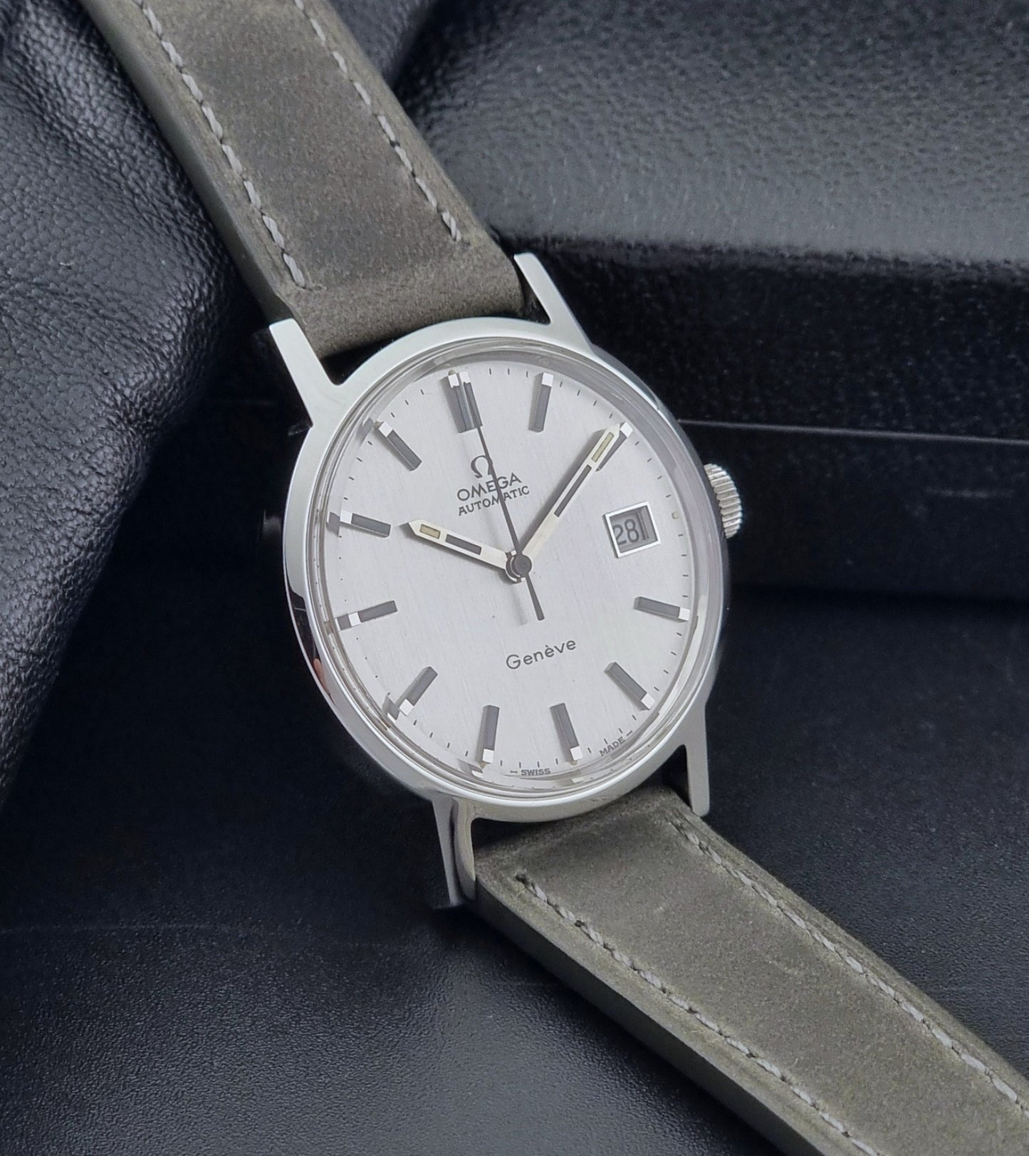 Vintage Omega Wristwatch Geneve 166.0098 with grey leather strap on a dark textured surface side view