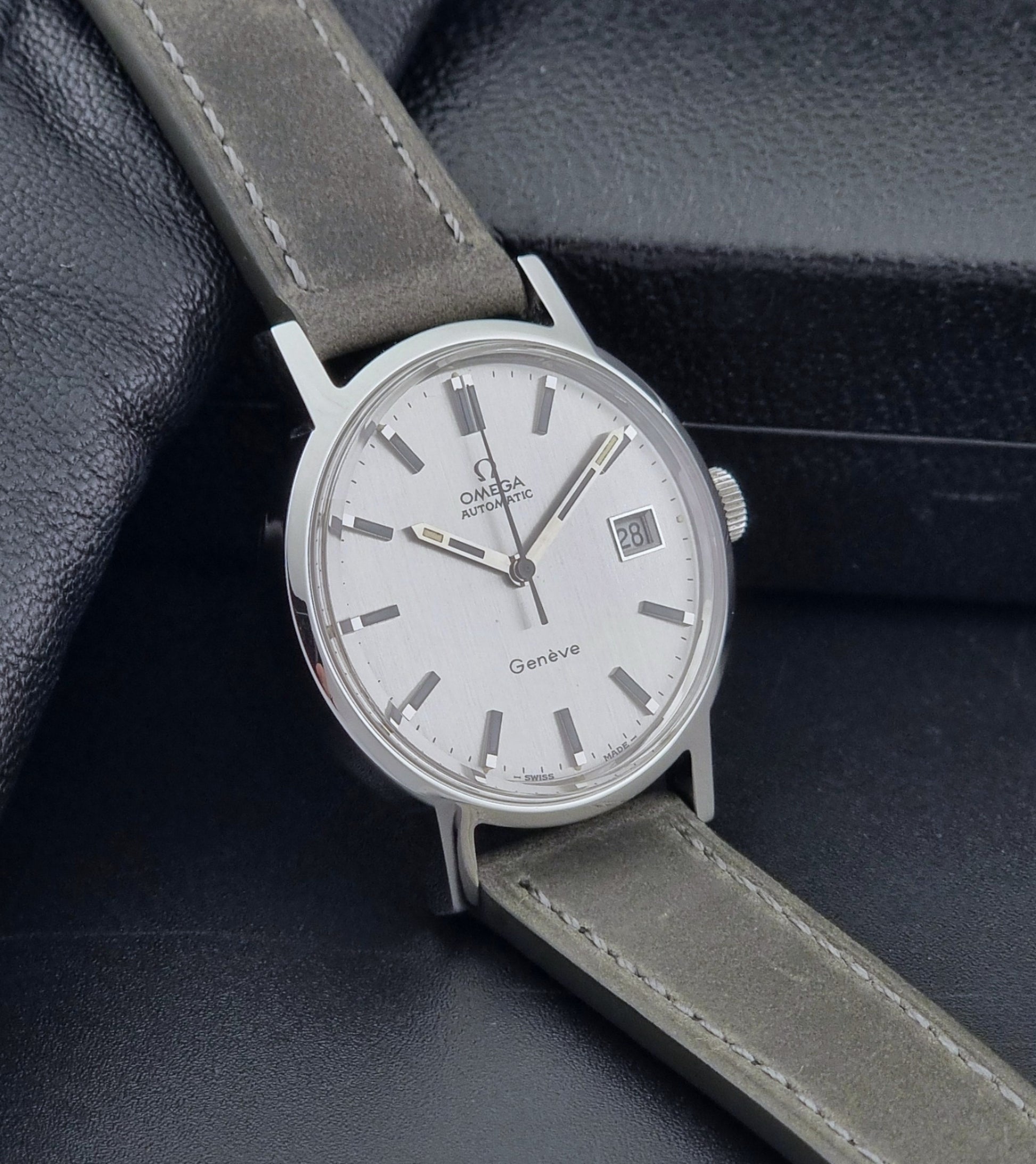 Vintage Omega Wristwatch Geneve 166.0098 with grey leather strap on a dark textured surface side view