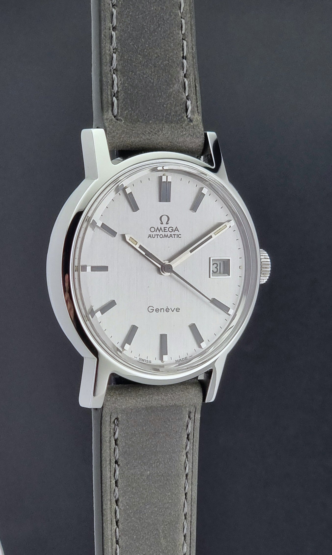 Vintage Omega Wristwatch Geneve 166.0098 with grey leather strap on a dark textured surface side profile view