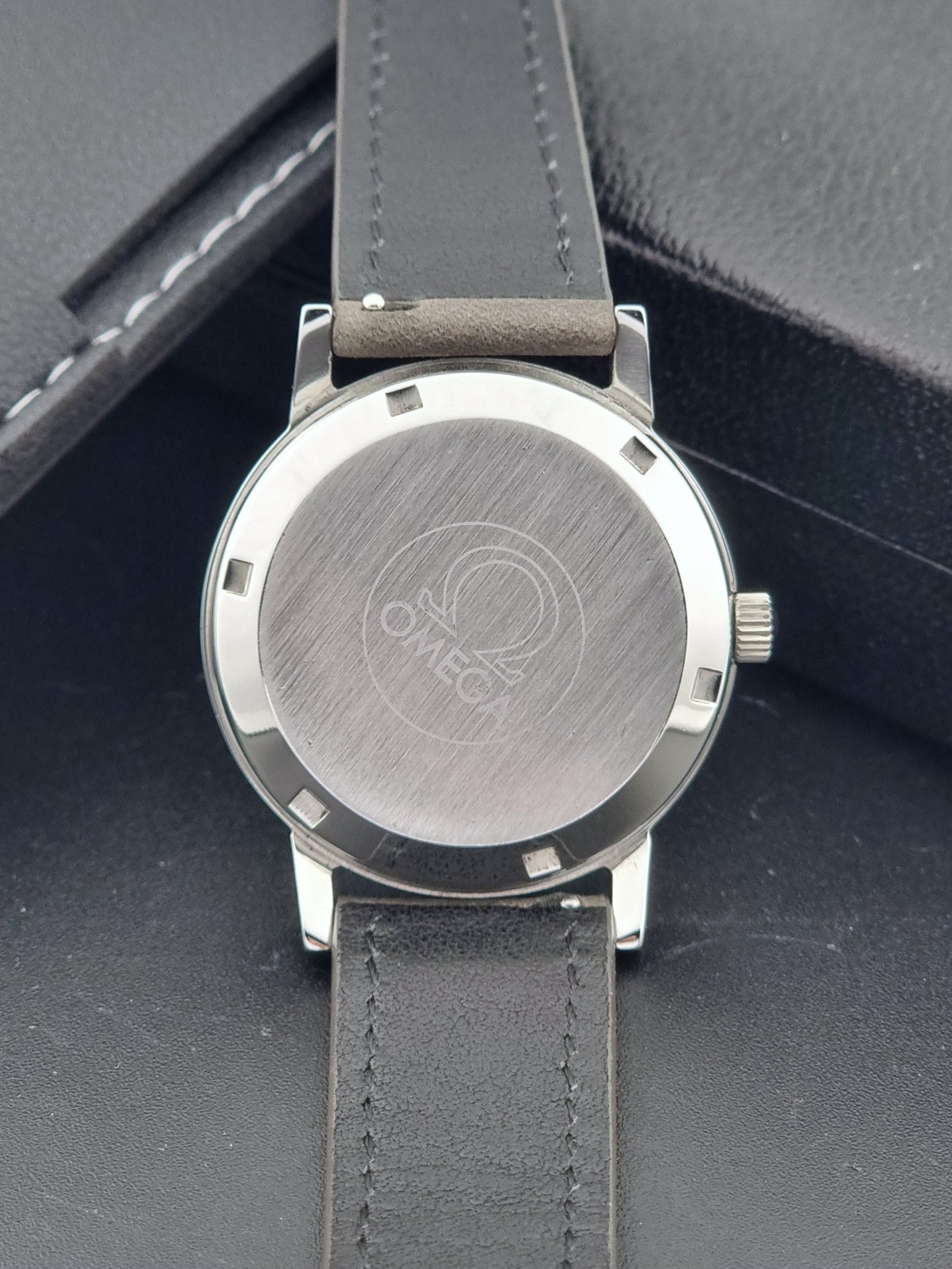Vintage Omega Geneve 166.0163 watch with gray leather strap on a dark background case back view