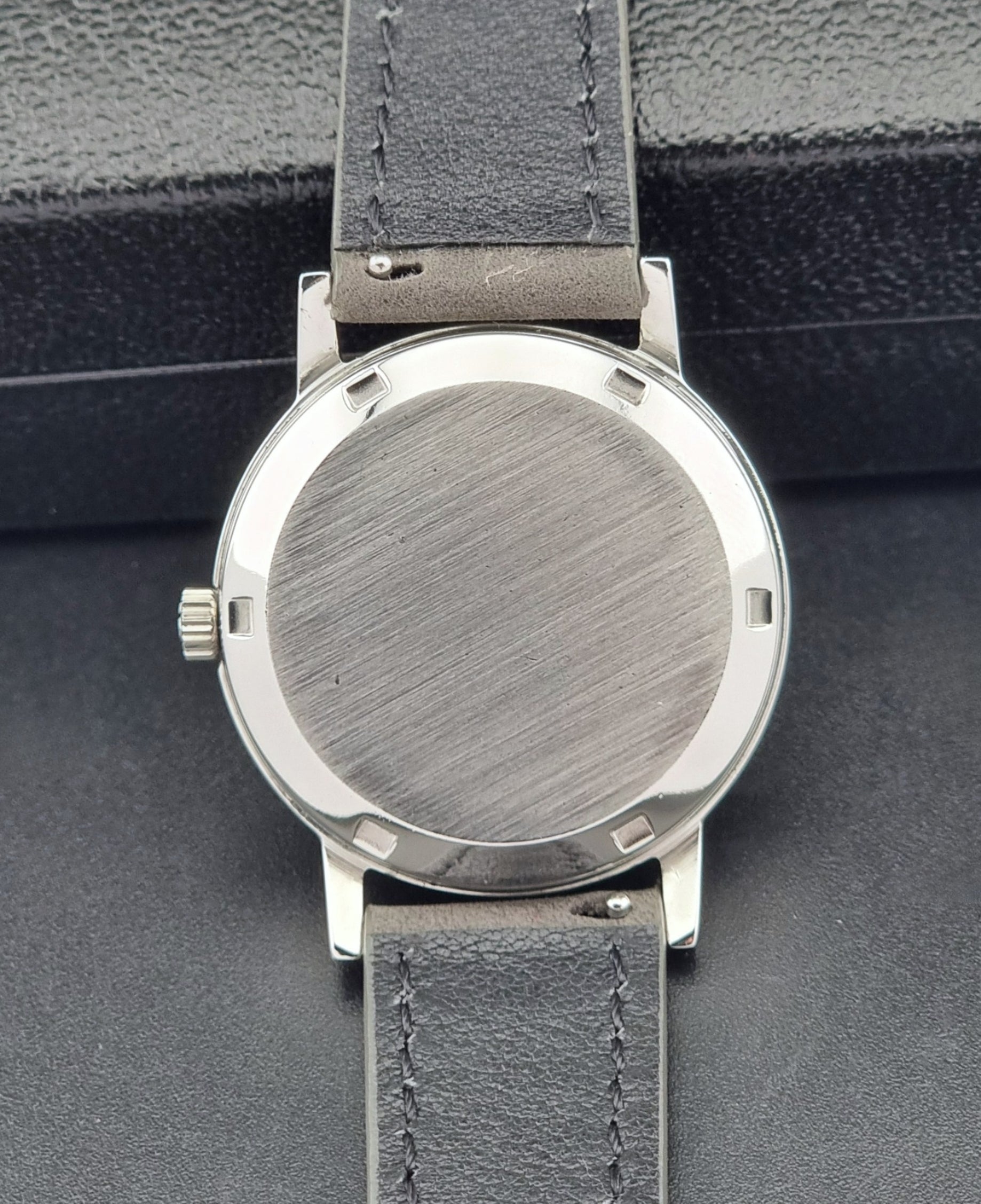 Vintage Omega case back with gray leather strap.